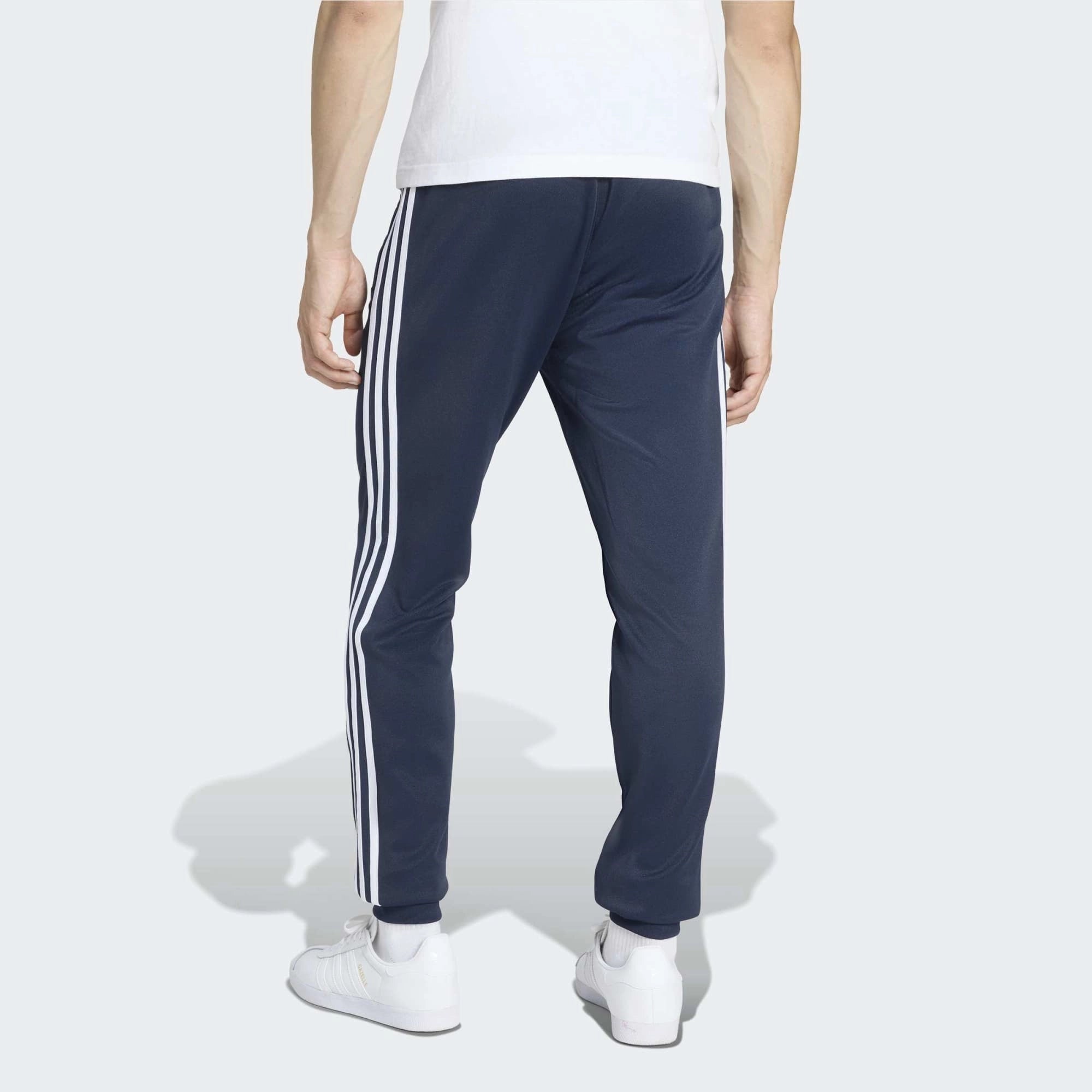 "Dunkelblaue adidas Originals SST Track Pant (Night Indigo) mit weißen 3-Streifen, Trefoil-Stickerei und Reißverschlusstaschen bei Stickabush Berlin."