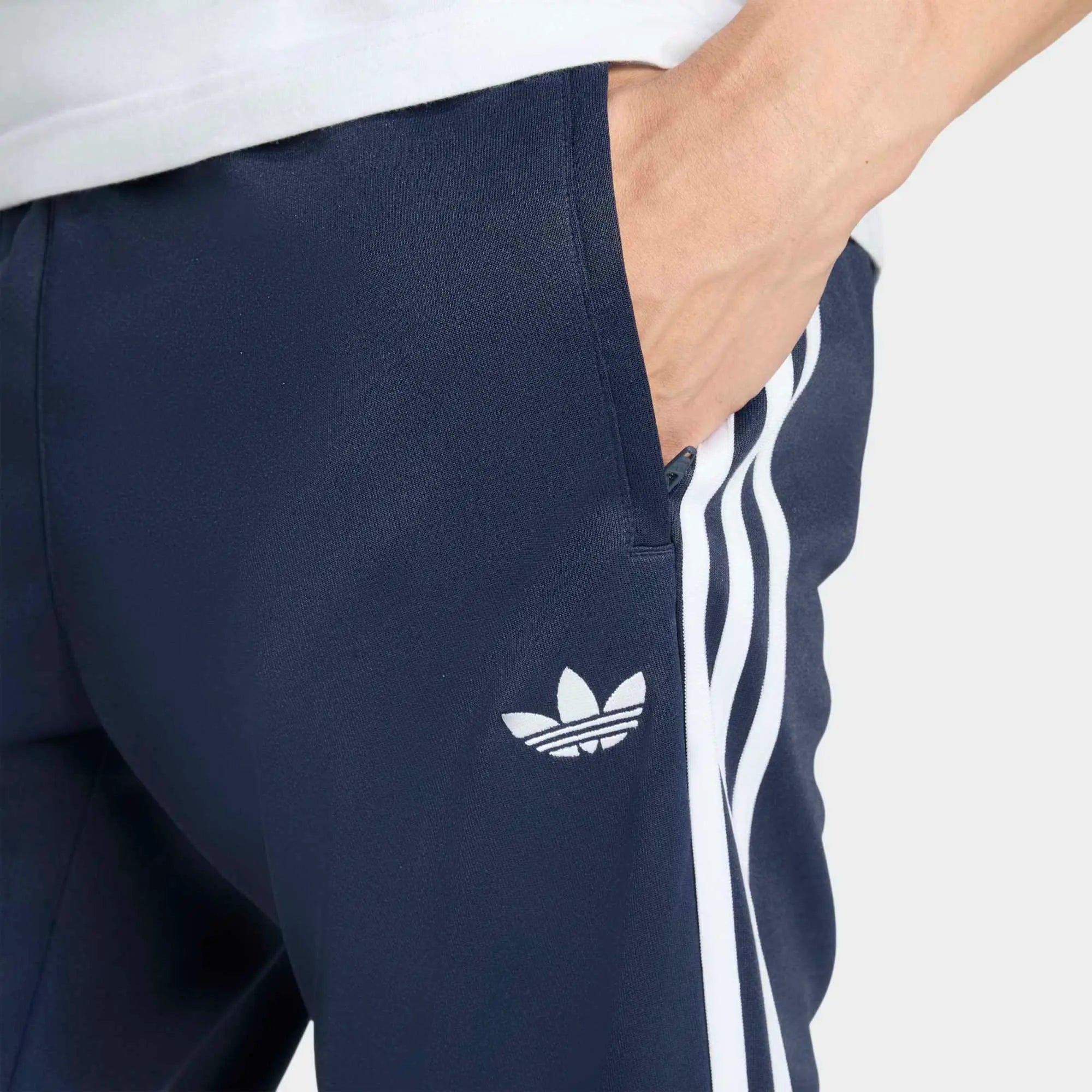 "Dunkelblaue adidas Originals SST Track Pant (Night Indigo) mit weißen 3-Streifen, Trefoil-Stickerei und Reißverschlusstaschen bei Stickabush Berlin."