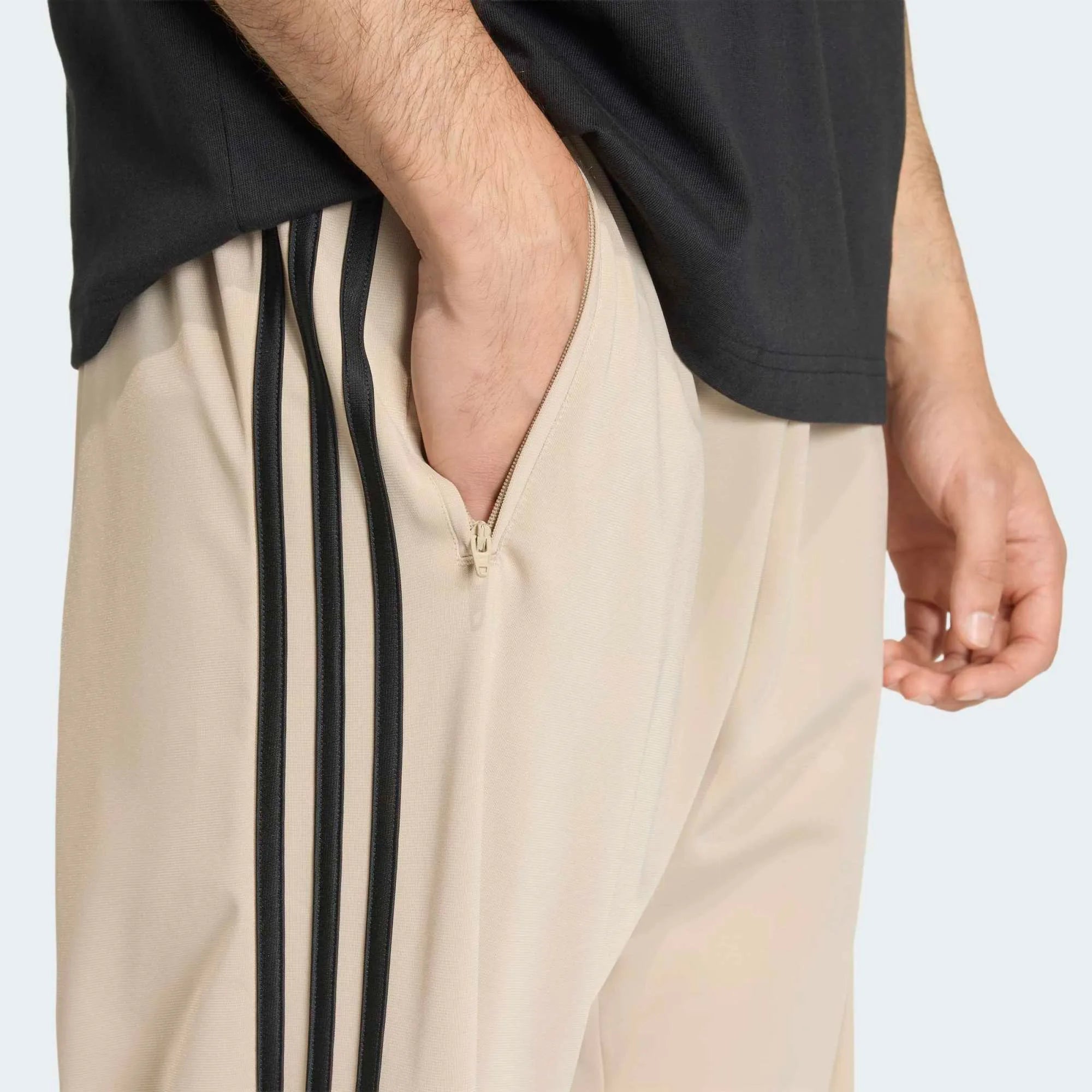 “Adidas Originals Firebird Track Pants in Stone Khaki mit schwarzen Streifen und gesticktem Trefoil-Logo bei Stickabush Berlin.“