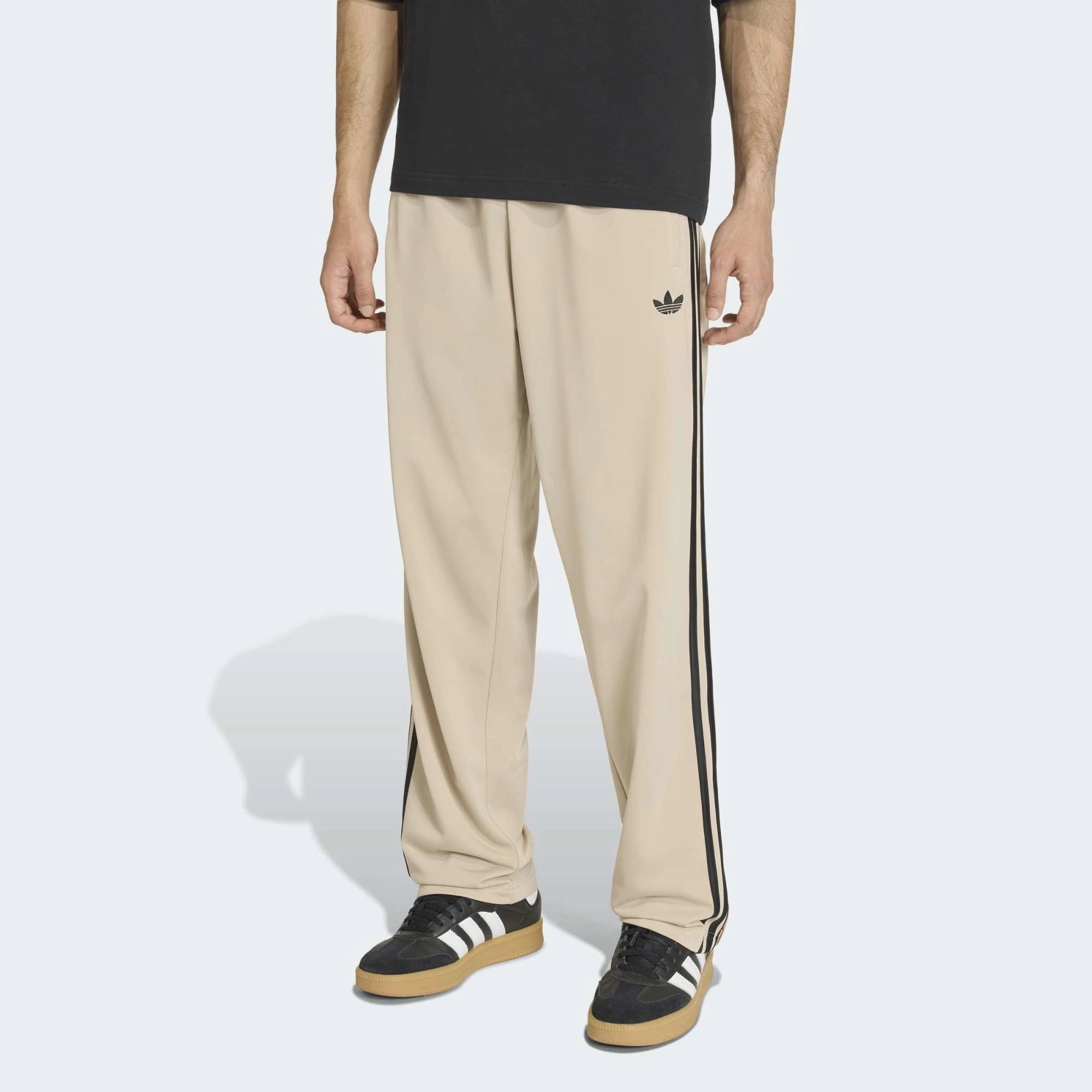 “Adidas Originals Firebird Track Pants in Stone Khaki mit schwarzen Streifen und gesticktem Trefoil-Logo bei Stickabush Berlin.“
