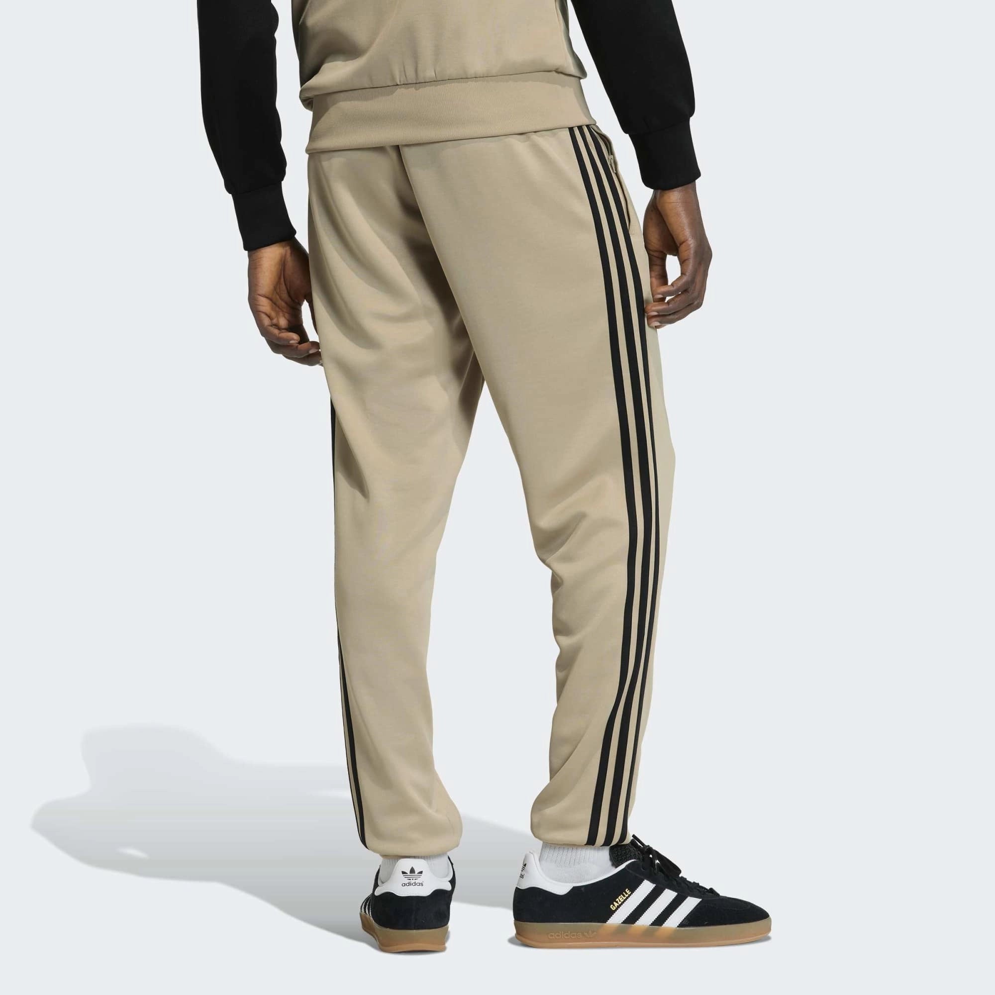 „Khakifarbene adidas Originals Classics SST Track Pants Trainingshose mit schwarzen 3-Streifen, gesticktem Trefoil-Logo und geradem Beinschnitt bei Stickabush Berlin.“