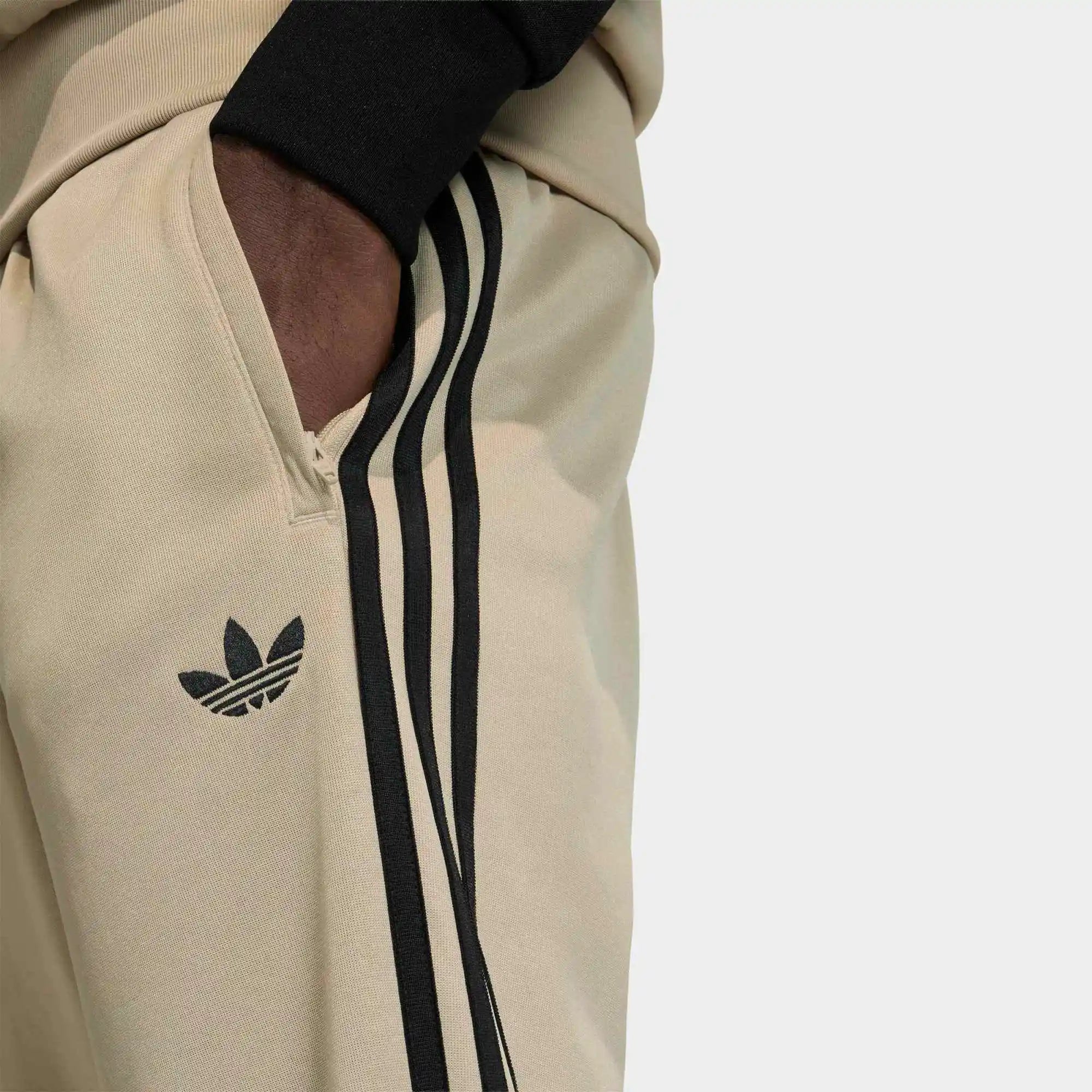 „Khakifarbene adidas Originals Classics SST Track Pants Trainingshose mit schwarzen 3-Streifen, gesticktem Trefoil-Logo und geradem Beinschnitt bei Stickabush Berlin.“