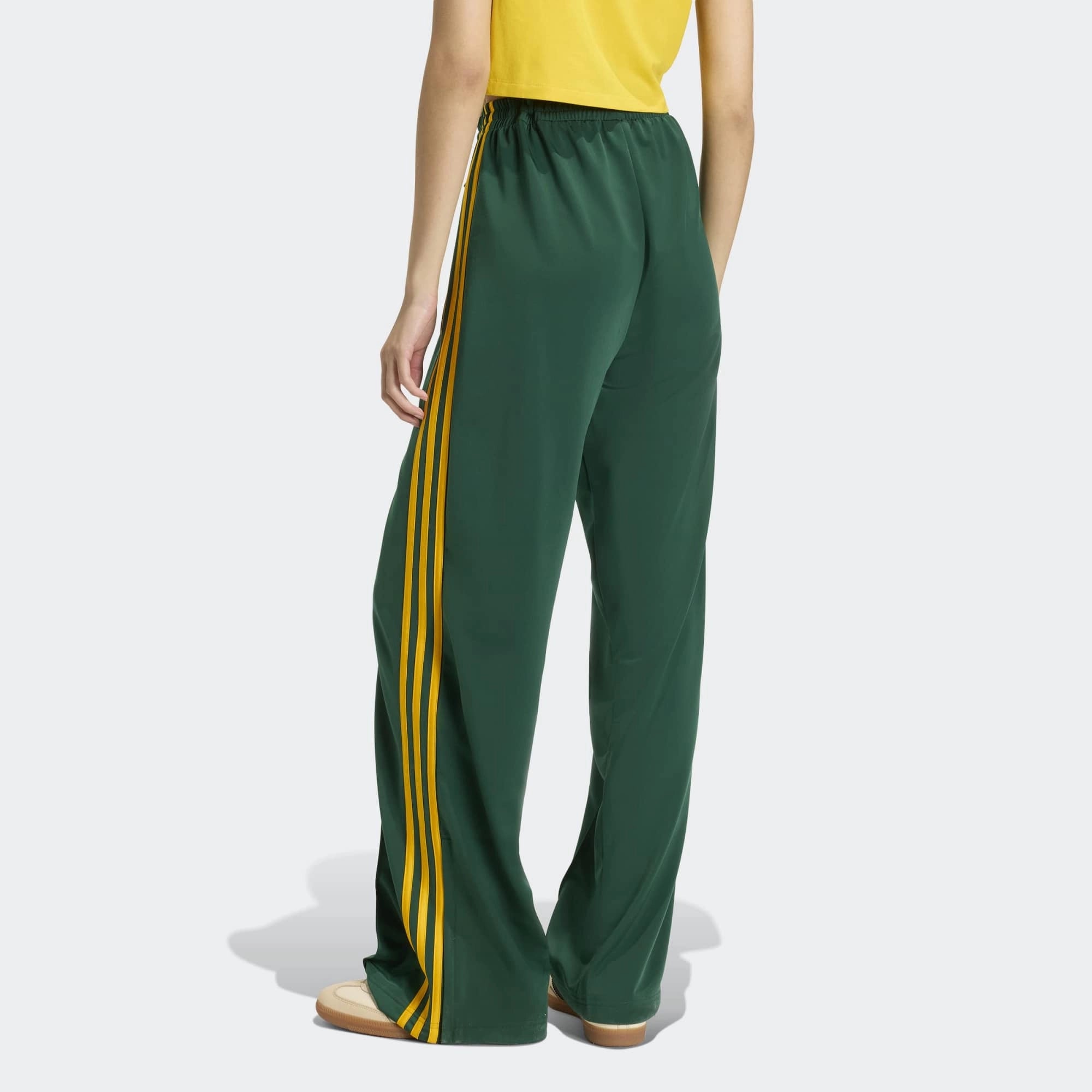 „Rückansicht Model der Adidas Originals Firebird Loose Track Pants W in Collegiate Green mit Crew Yellow 3-Streifen – Weit geschnittene Damen-Trainingshose aus glänzendem Trikot bei Stickabush Berlin.“