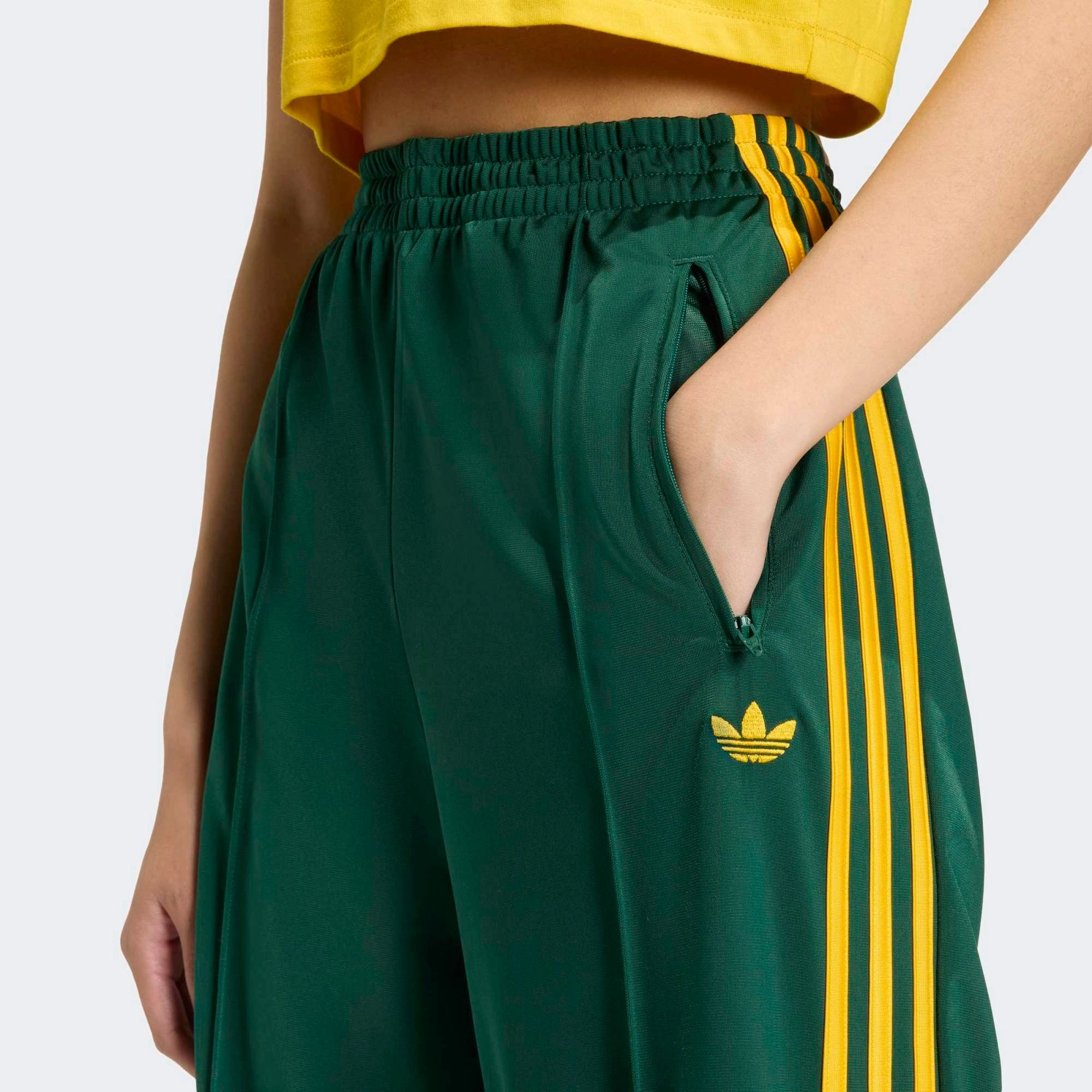 „Frontansicht Model Detail der Adidas Originals Firebird Loose Track Pants W in Collegiate Green mit Crew Yellow 3-Streifen – Weit geschnittene Damen-Trainingshose aus glänzendem Trikot bei Stickabush Berlin.“