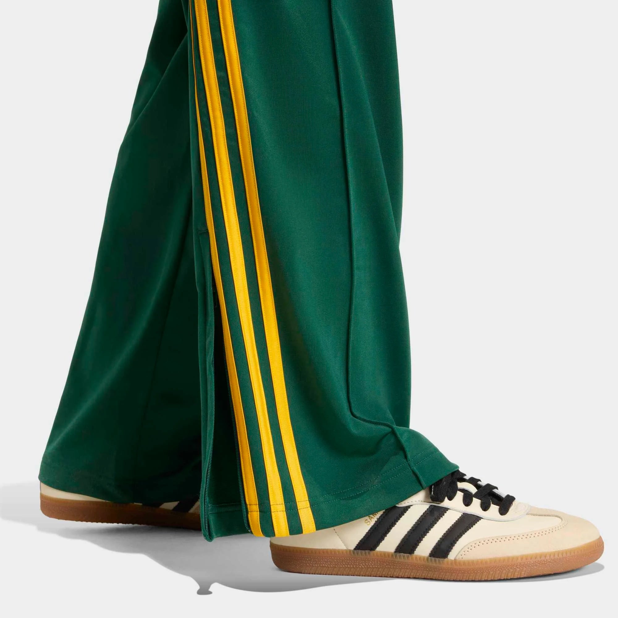 „Seitenansicht Model Detail der Adidas Originals Firebird Loose Track Pants W in Collegiate Green mit Crew Yellow 3-Streifen – Weit geschnittene Damen-Trainingshose aus glänzendem Trikot bei Stickabush Berlin.“