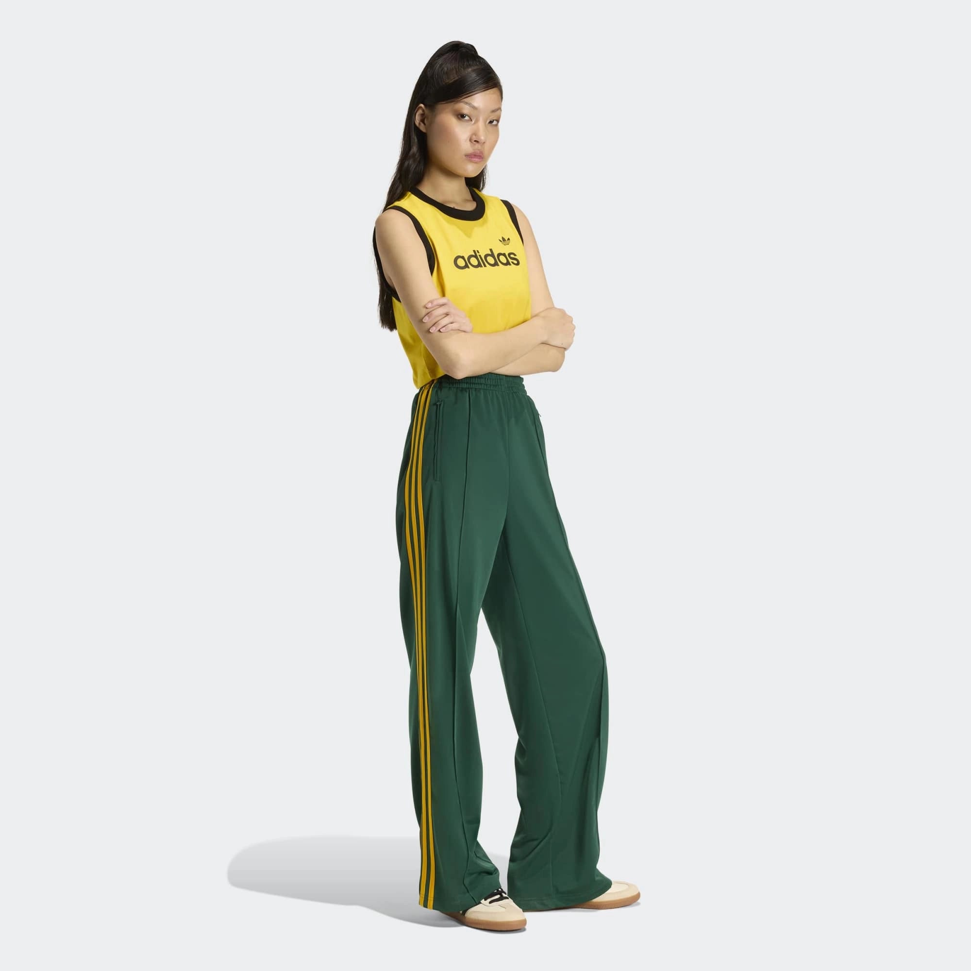 „Frontansicht Model Outfit der Adidas Originals Firebird Loose Track Pants W in Collegiate Green mit Crew Yellow 3-Streifen – Weit geschnittene Damen-Trainingshose aus glänzendem Trikot bei Stickabush Berlin.“