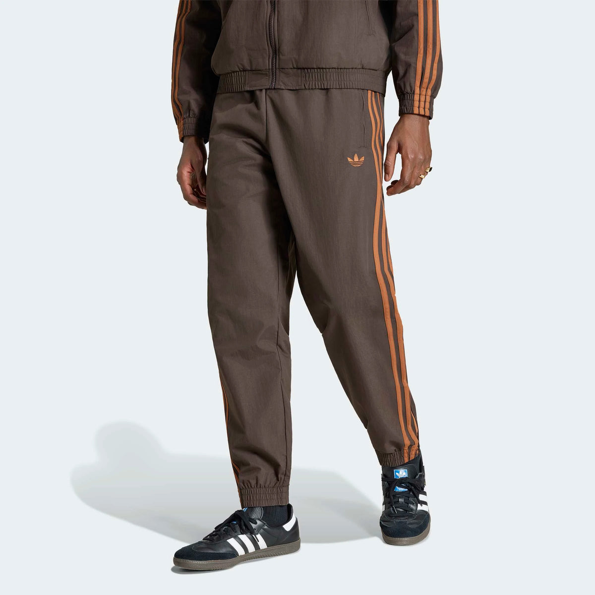 adidas Originals Firebird Woven Track Pants in Aurora Coffee – Frontansicht am Model der braunen Trainingshose aus Webmaterial mit den ikonischen 3-Stripes.