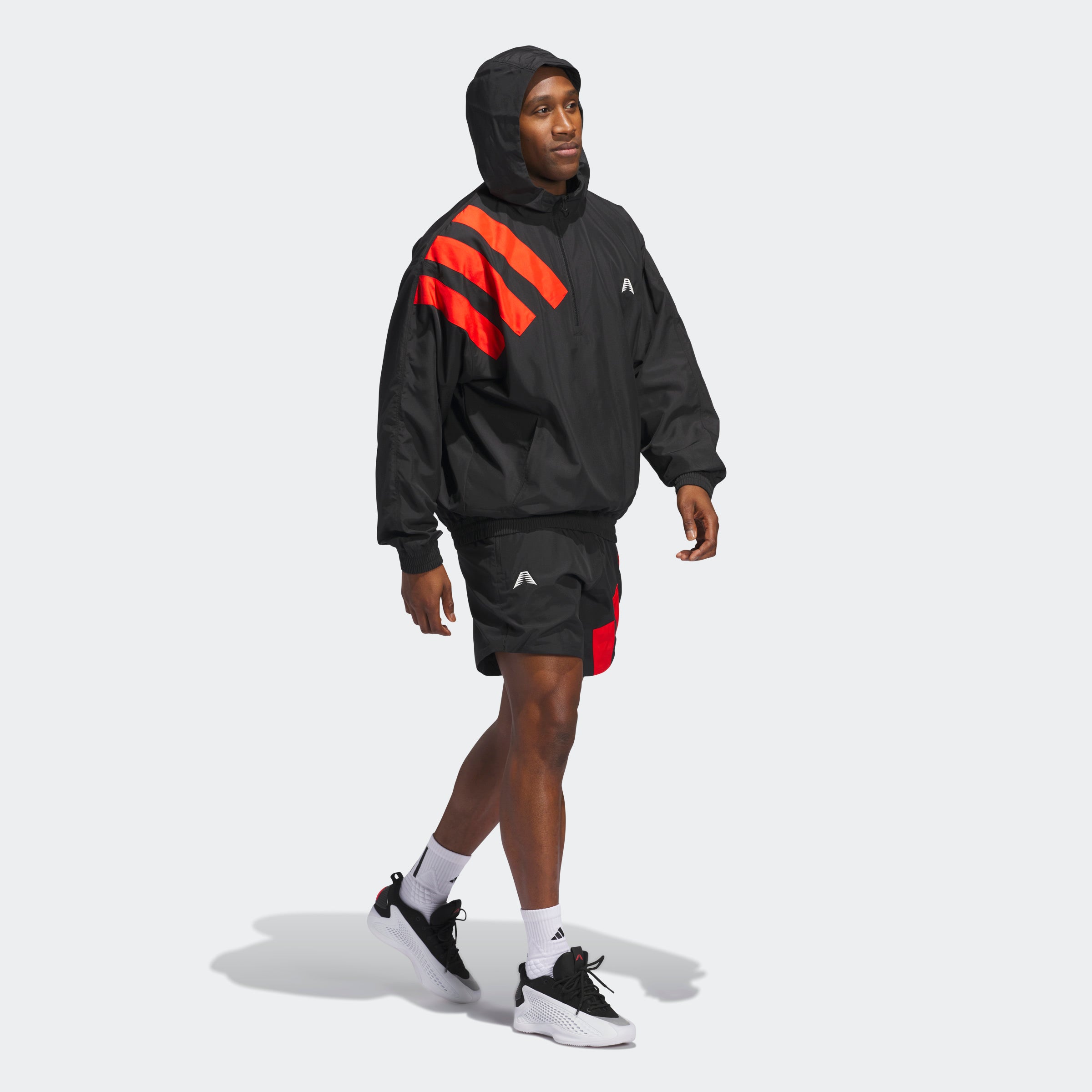 “The Adidas Originals Anthony Edwards Anorak Pullover in black, JC8782, features a hooded design with three bold red diagonal stripes on the upper left shoulder. Made from recycled materials, this durable nylon pullover includes a halfway zipper, white chest logo, and elastic cuffs and waistband for a snug fit.“