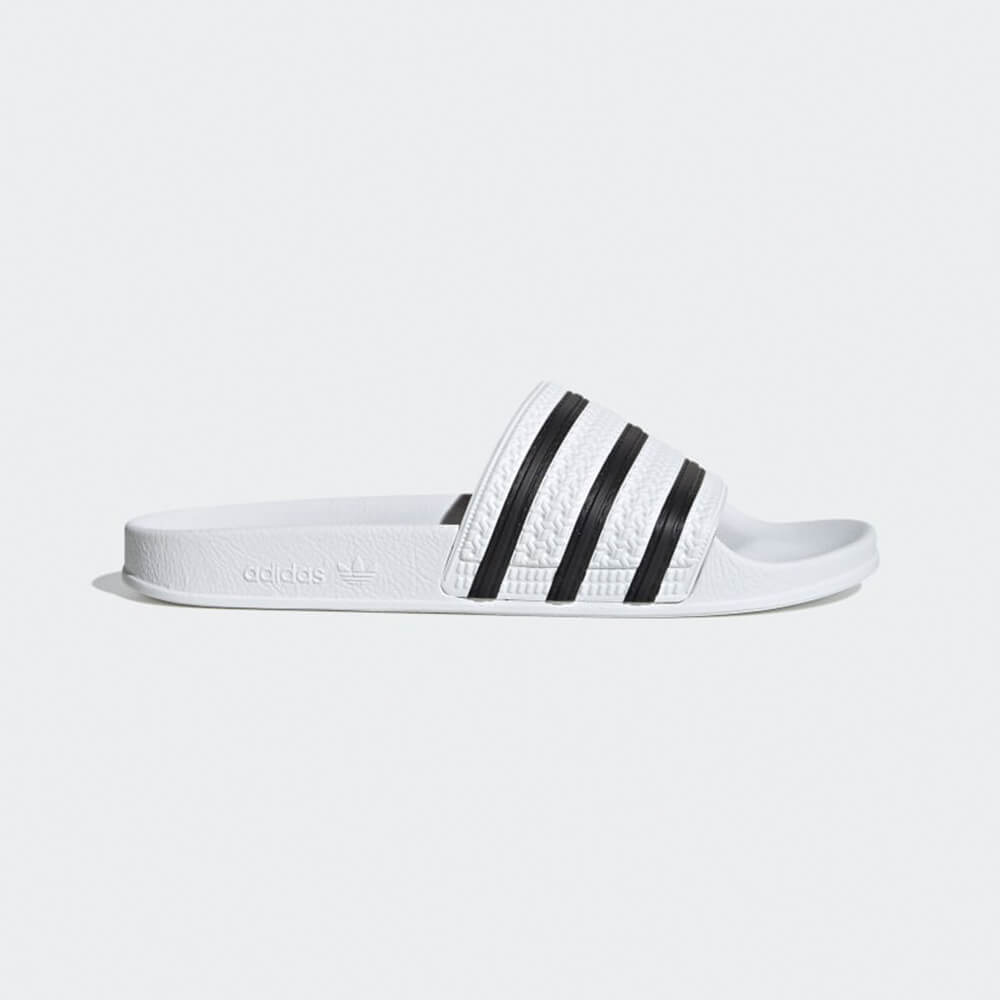 “Seitenansicht der Adidas Originals Adilette in White / Black – Klassische Badeschlappen mit weißen 3-Streifen auf schwarzem Riemen und vorgeformtem Fußbett bei Stickabush Berlin.“