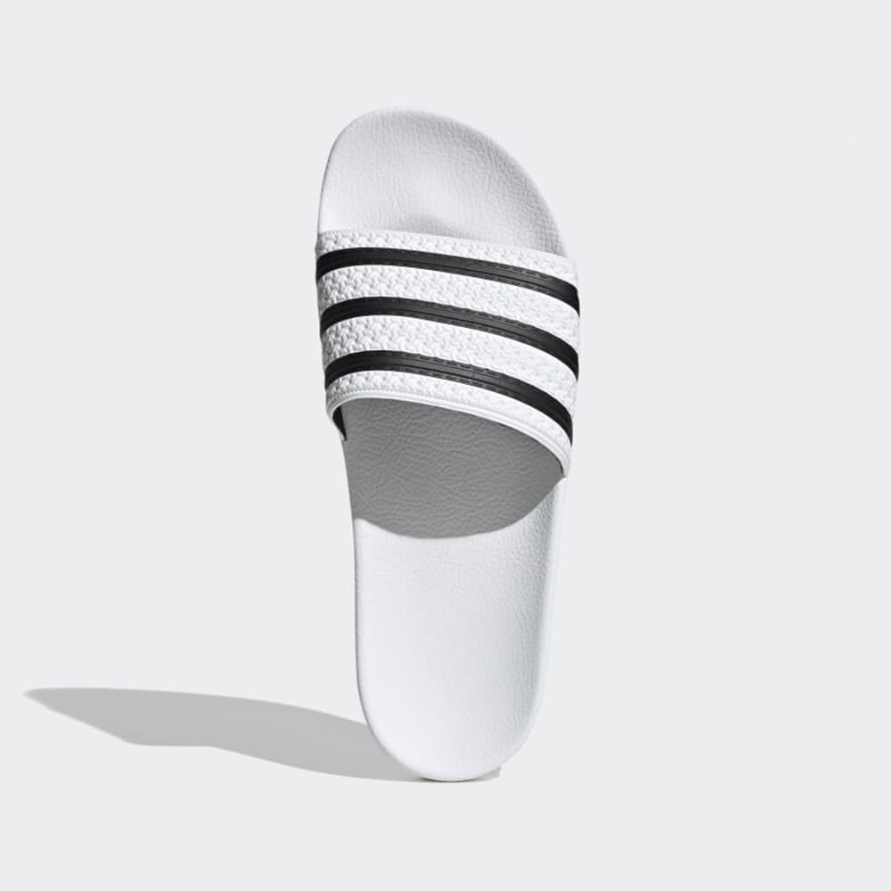 “Vogelansicht der Adidas Originals Adilette in White / Black – Klassische Badeschlappen mit weißen 3-Streifen auf schwarzem Riemen und vorgeformtem Fußbett bei Stickabush Berlin.“