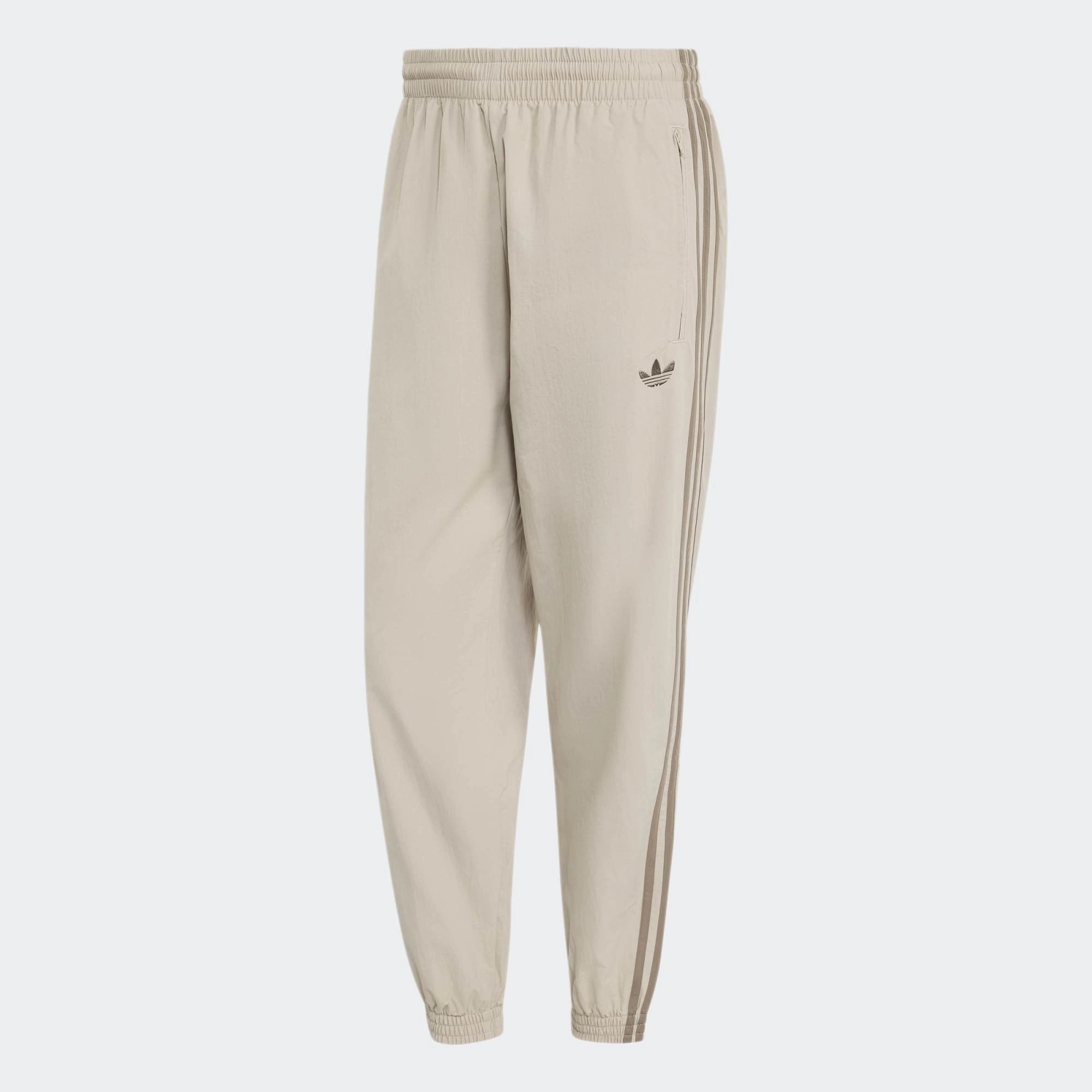 „Beigefarbene adidas Originals Firebird Woven Track Pants (KS7503) aus gewebtem Material mit weißen Streifen – leichte Damen-Trainingshose im Retro-Stil erhältlich bei Stickabush Berlin.“