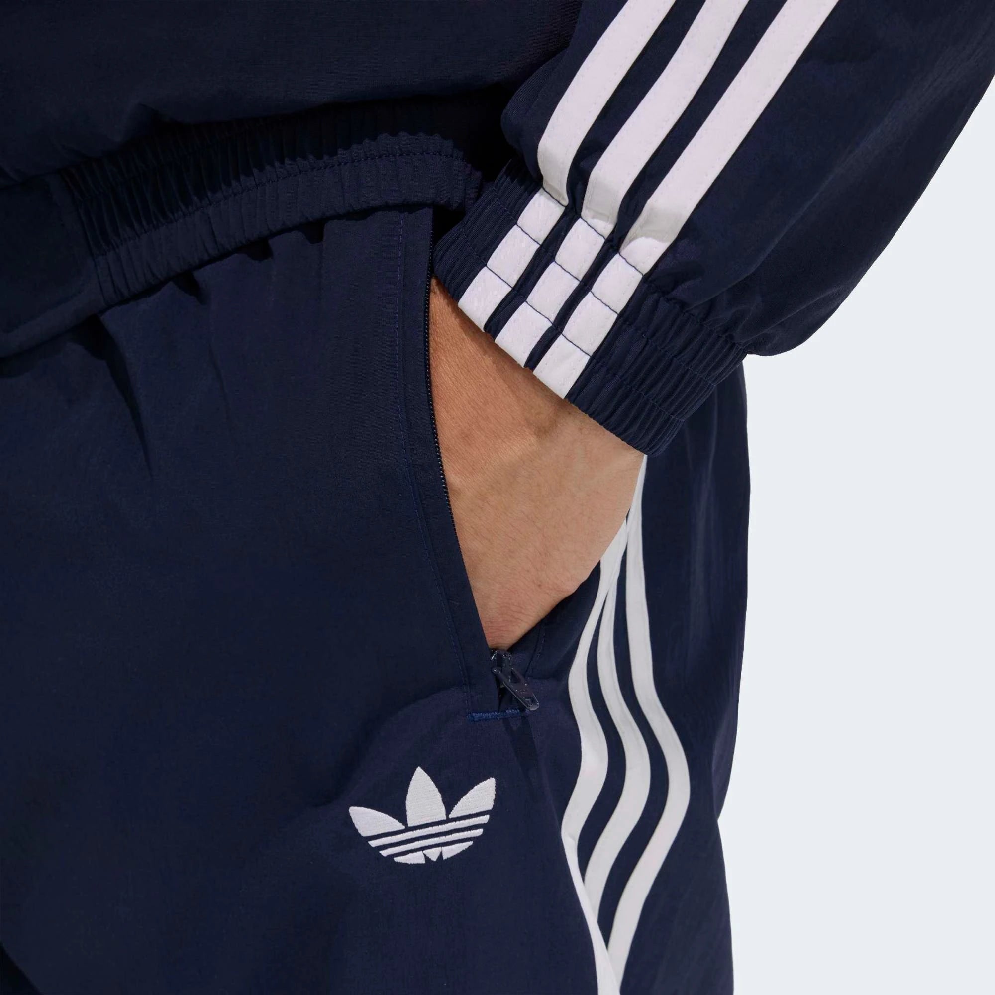 “Die adidas Originals Firebird Woven Trainingshose in Night Indigo (Dunkelblau) mit weißen 3-Streifen und leichtes, strapazierfähiges Webmaterial (Woven) bei Stickabush“.