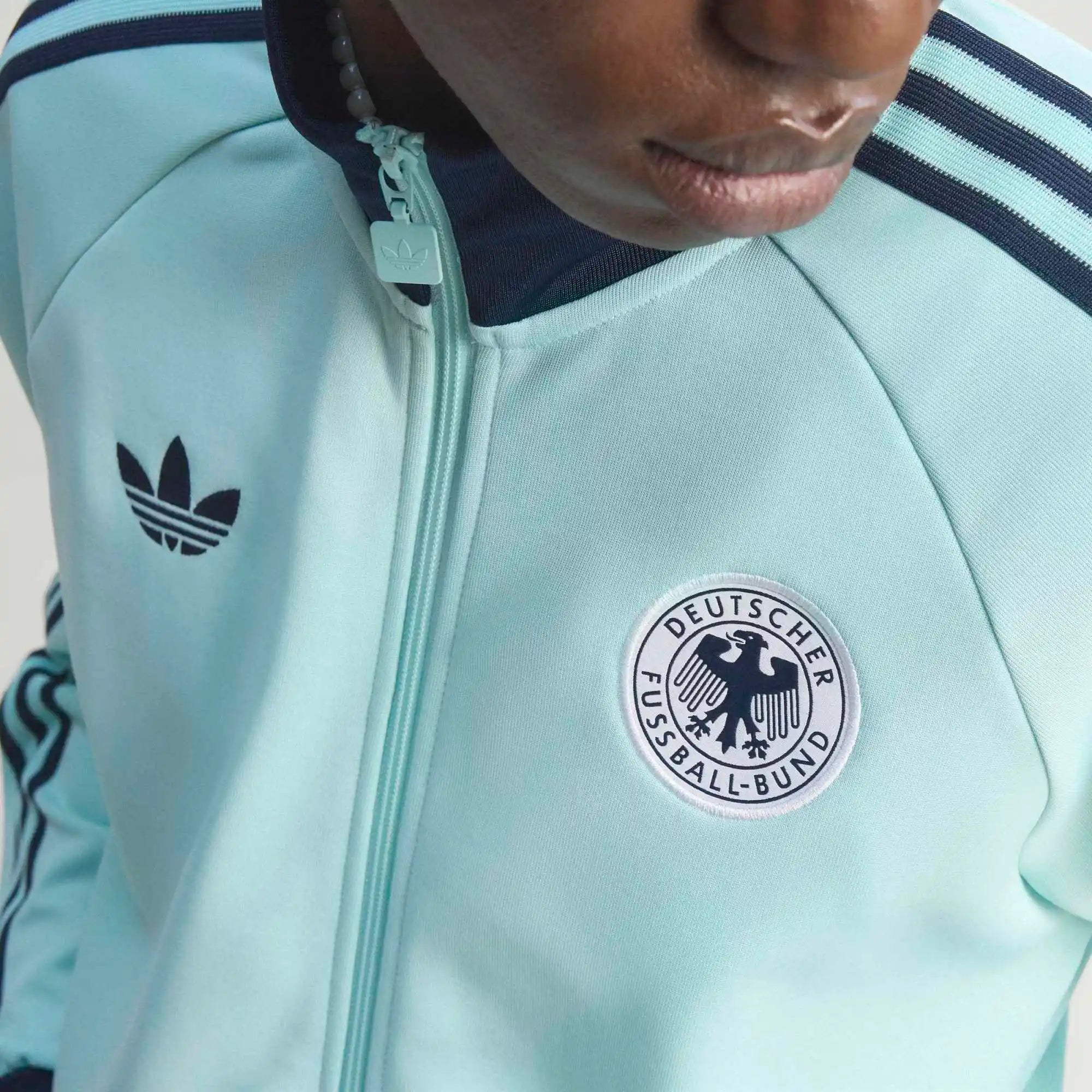 “Die türkise adidas Originals Deutschland OG Trainingsjacke (Semi Flash Aqua) mit klassischen weißen 3-Streifen und Retro-Details bei Stickabush“.