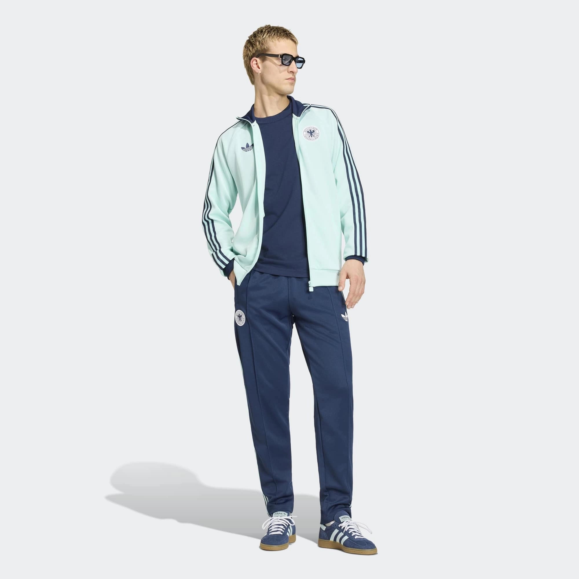 “Die türkise adidas Originals Deutschland OG Trainingsjacke (Semi Flash Aqua) mit klassischen weißen 3-Streifen und Retro-Details bei Stickabush“.