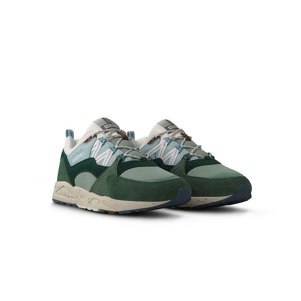 „Der Karhu Fusion 2.0 Mölkky Pack in Laurel Wreath / Blanc de Blanc ist ein Retro-Sneaker mit dunkel- und hellgrünen Elementen, beigen Akzenten und einer beigen Sohle. An der Seite befindet sich das elegante Karhu-Branding.“