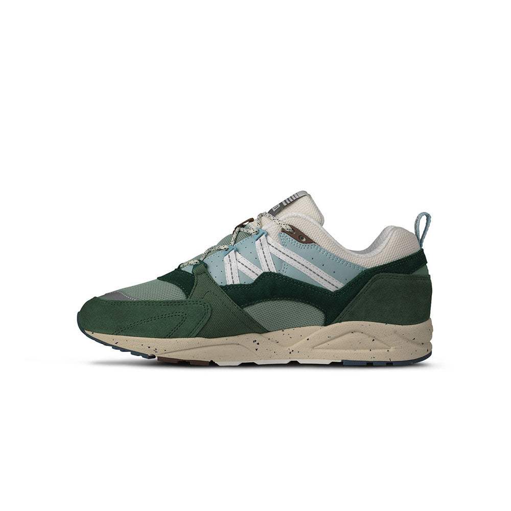 „Der Karhu Fusion 2.0 Mölkky Pack in Laurel Wreath / Blanc de Blanc ist ein Retro-Sneaker mit dunkel- und hellgrünen Elementen, beigen Akzenten und einer beigen Sohle. An der Seite befindet sich das elegante Karhu-Branding.“