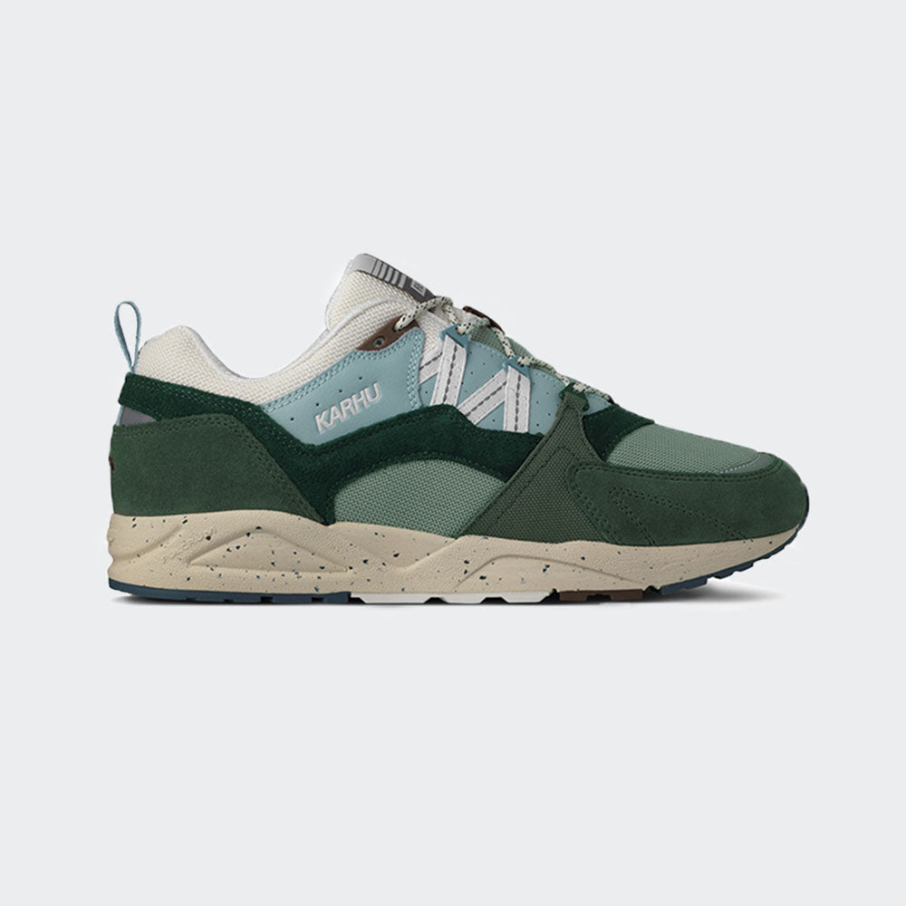 „Der Karhu Fusion 2.0 Mölkky Pack in Laurel Wreath / Blanc de Blanc ist ein Retro-Sneaker mit dunkel- und hellgrünen Elementen, beigen Akzenten und einer beigen Sohle. An der Seite befindet sich das elegante Karhu-Branding.“