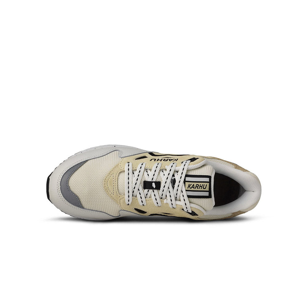 “Die Karhu Legacy 96 - Blanc de Blanc, Sneakers präsentieren sich in einem beigen und hellgrauen Design mit schwarzen Akzenten. Sie verfügen über weiße Schnürsenkel, eine klobige Sohle, einen perforierten Zehenbereich und einen strukturierten Absatz.“
