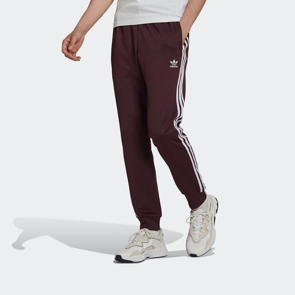 "Adidas Classics SST Track Pants in Weinrot, HK7352, aus Polyester/Baumwolle, schmal geschnitten, klassische adidas Trainingshose mit Streifen."