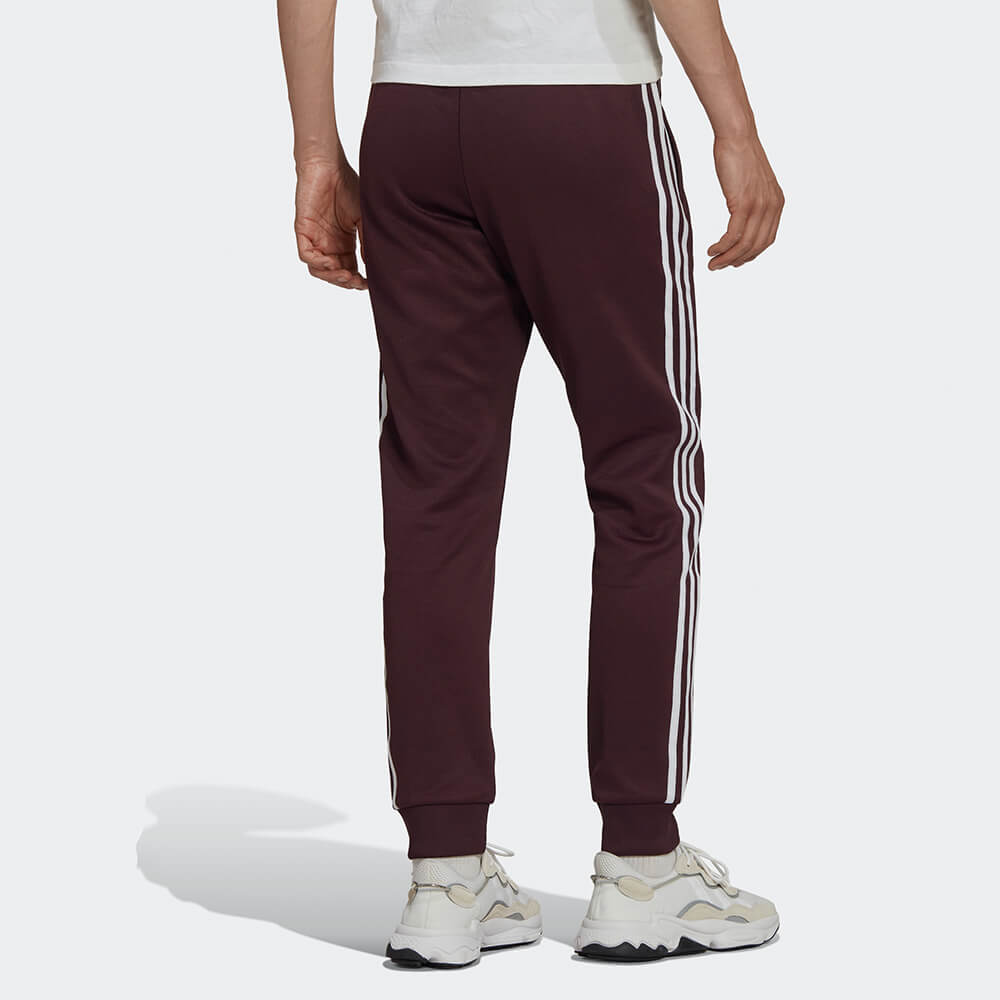 "Adidas Classics SST Track Pants in Weinrot, HK7352, aus Polyester/Baumwolle, schmal geschnitten, klassische adidas Trainingshose mit Streifen."