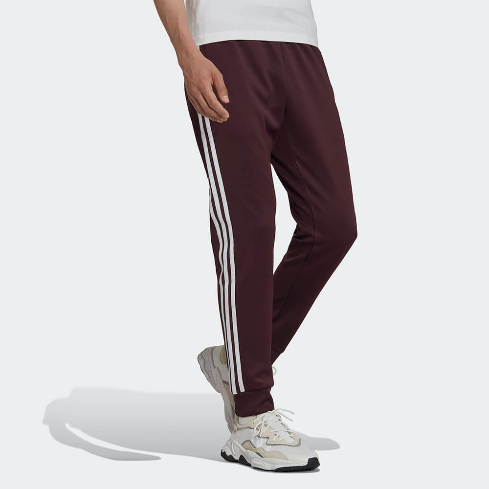 "Adidas Classics SST Track Pants in Weinrot, HK7352, aus Polyester/Baumwolle, schmal geschnitten, klassische adidas Trainingshose mit Streifen."
