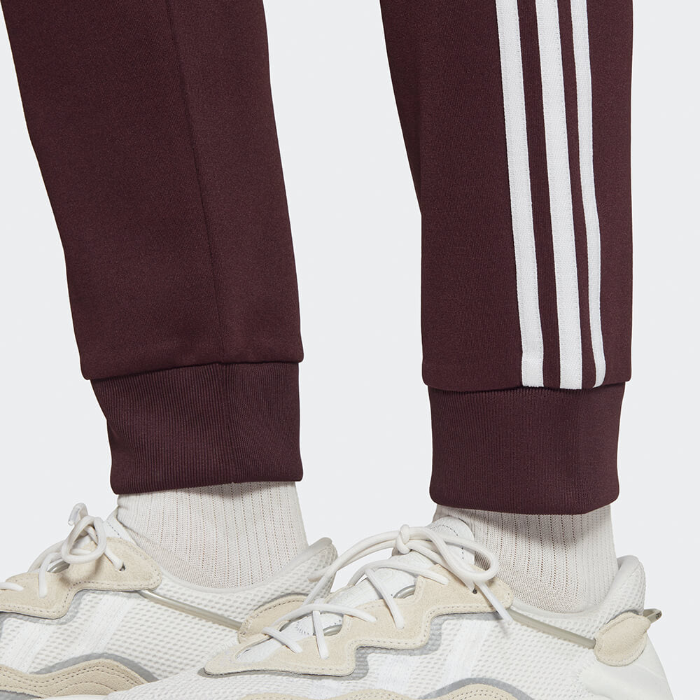 "Adidas Classics SST Track Pants in Weinrot, HK7352, aus Polyester/Baumwolle, schmal geschnitten, klassische adidas Trainingshose mit Streifen."