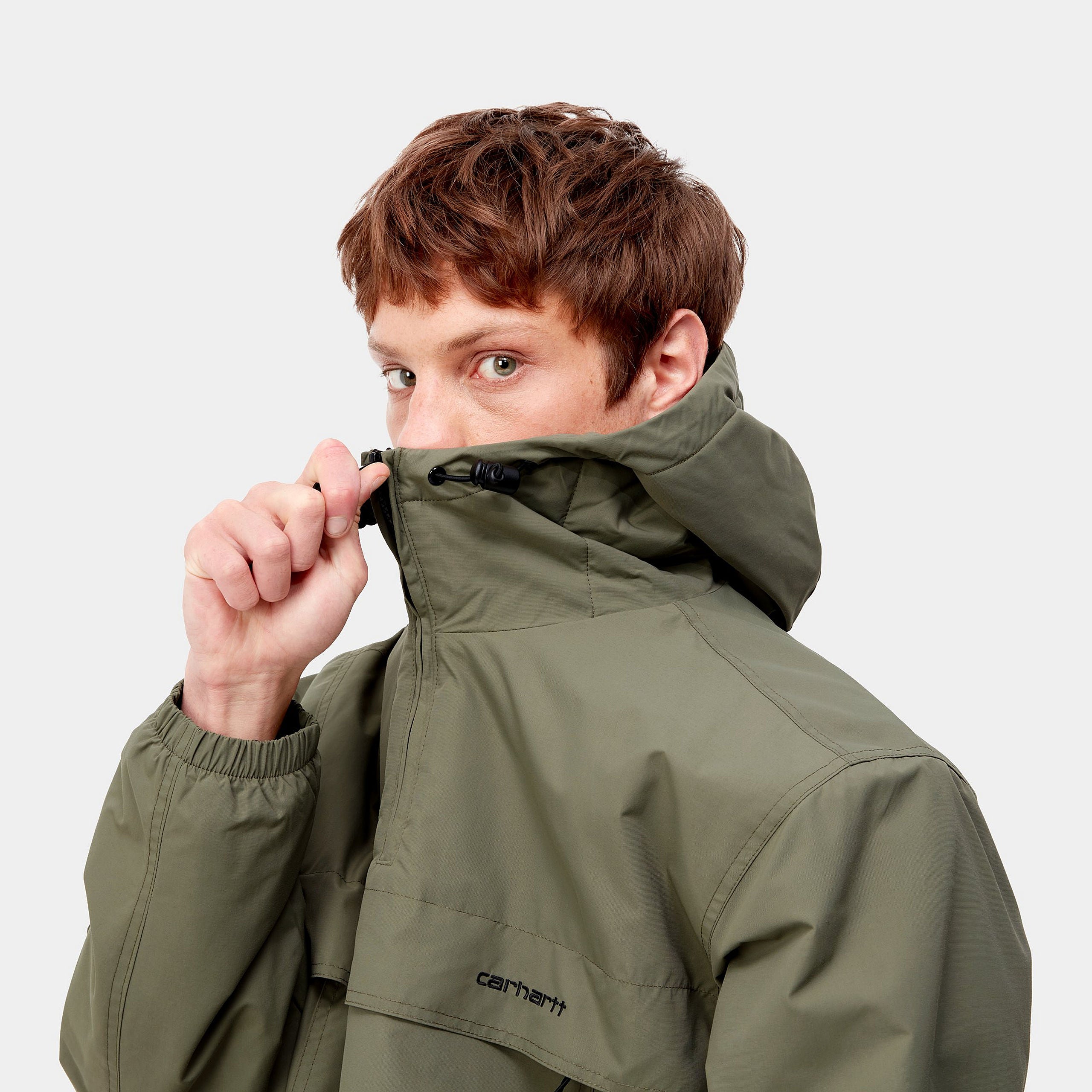 Carhartt WIP Windbreaker Pullover (Winter) – Seaweed / Black. Grüner Winter-Windbreaker aus Nylon mit Fleece-Futter, Kapuze, halbem Reißverschluss und schwarzer Logostickerei.