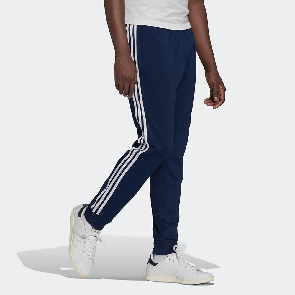 "Dunkelblaue adidas Originals SST Track Pant (Night Indigo) mit weißen 3-Streifen, Trefoil-Stickerei und Reißverschlusstaschen bei Stickabush Berlin."
