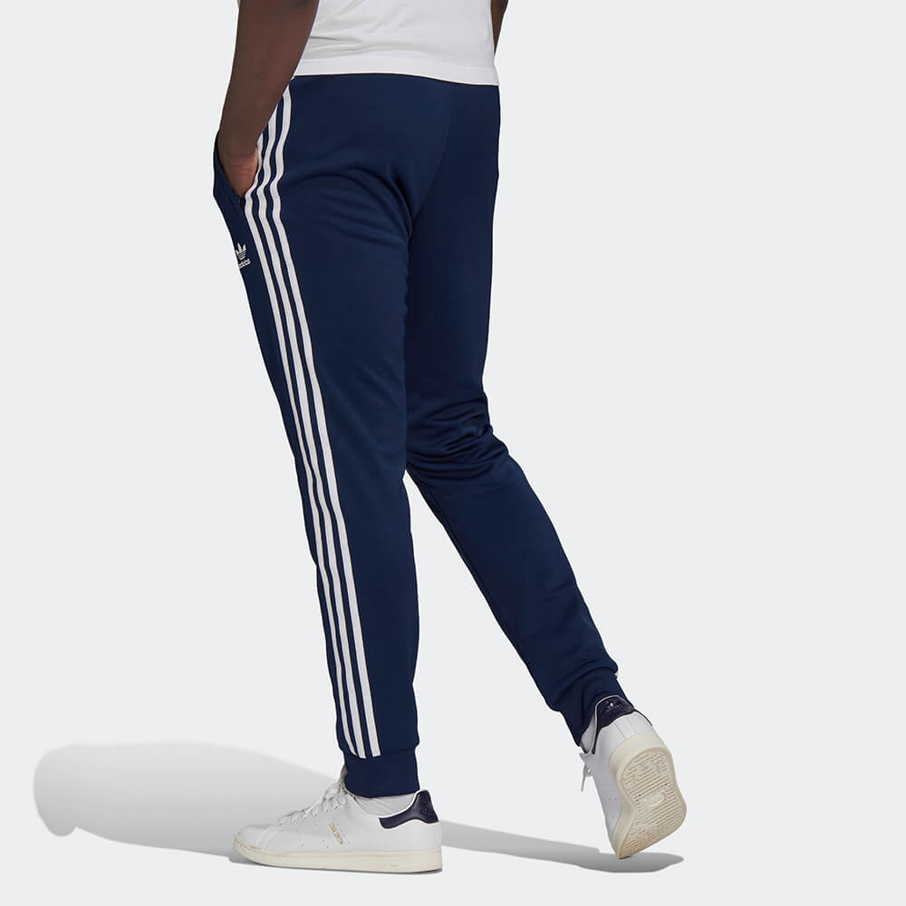 "Dunkelblaue adidas Classics SST Track Pant (Night Indigo) mit weißen 3-Streifen, Trefoil-Stickerei und Reißverschlusstaschen bei Stickabush Berlin."