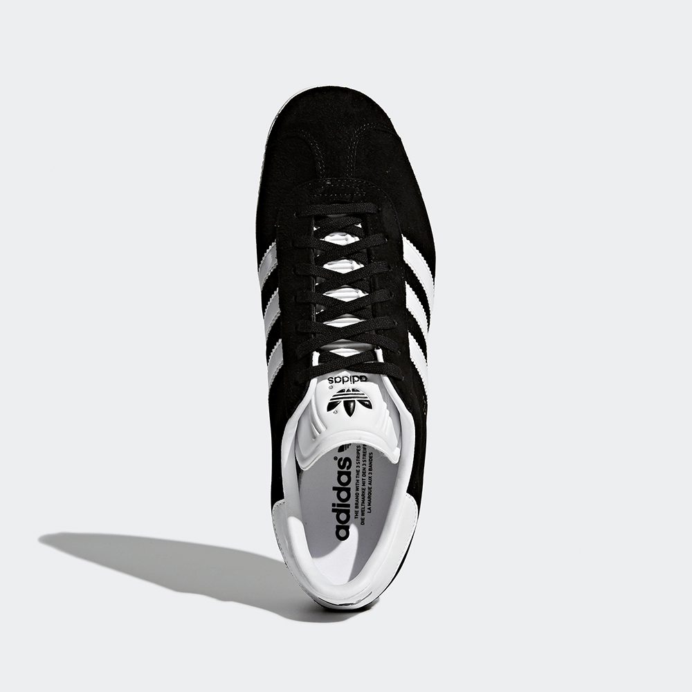 "Adidas Gazelle, Core Black/Footwear White, Wildleder, klassischer Sneaker in Schwarz mit weißen Streifen und goldener 'Gazelle'-Aufschrift."
