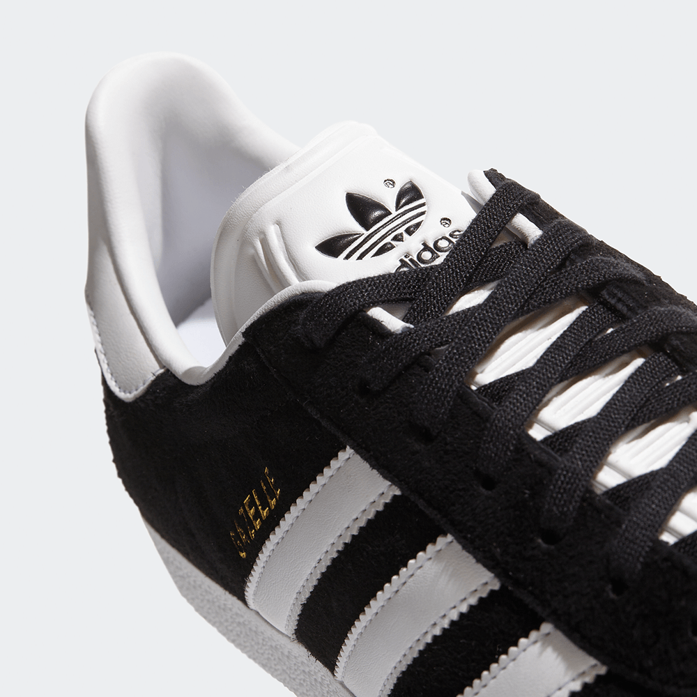 "Adidas Gazelle, Core Black/Footwear White, Wildleder, klassischer Sneaker in Schwarz mit weißen Streifen und goldener 'Gazelle'-Aufschrift."