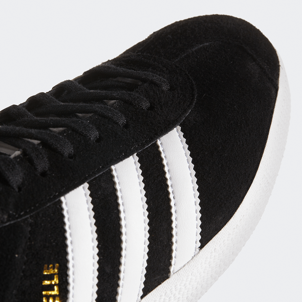 "Adidas Gazelle, Core Black/Footwear White, Wildleder, klassischer Sneaker in Schwarz mit weißen Streifen und goldener 'Gazelle'-Aufschrift."