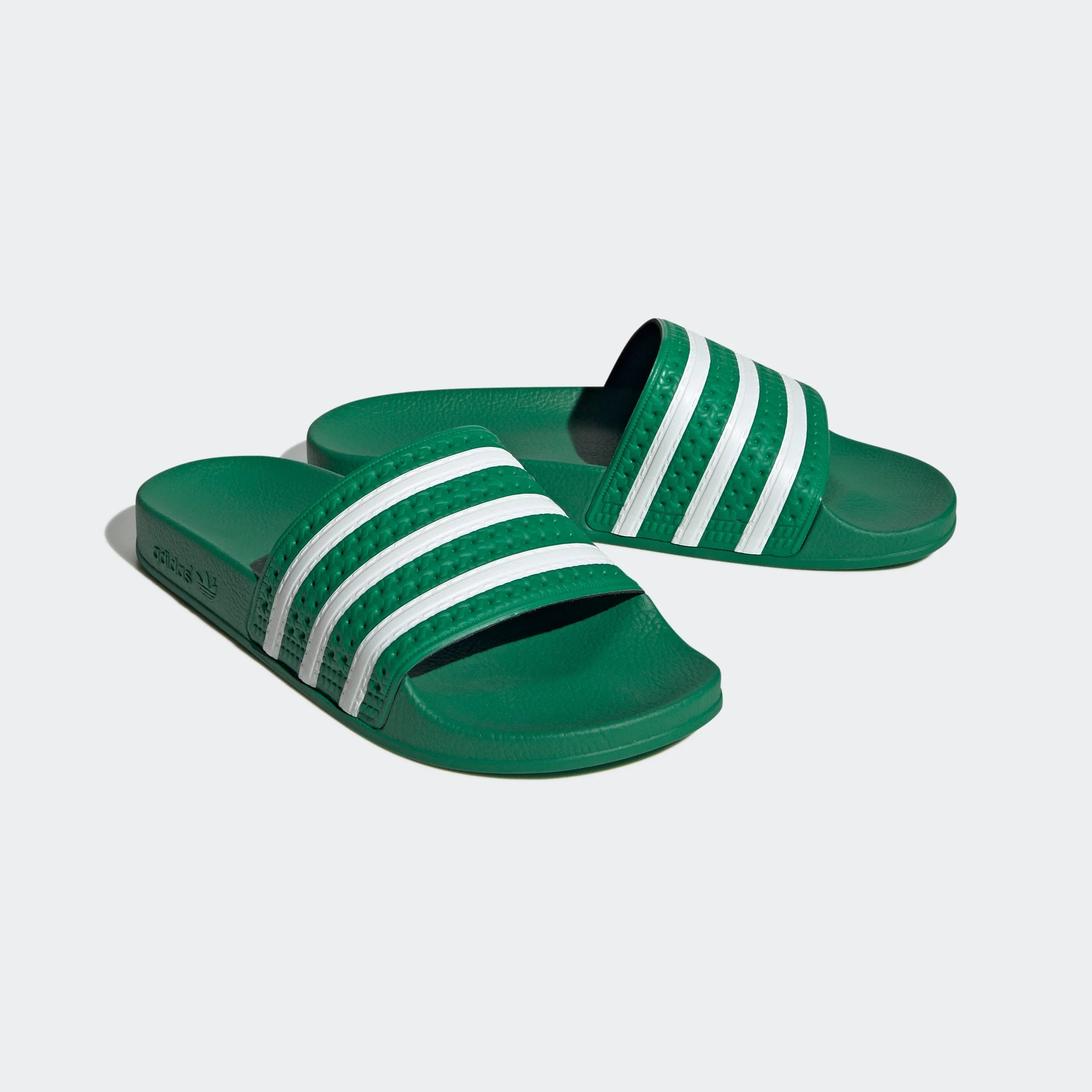 "Grüne Adidas Adilette für Damen mit weißen Details. Klassische Badesandale mit breitem Riemen und weißem Adidas Logo. Bequemes, leichtes Material."