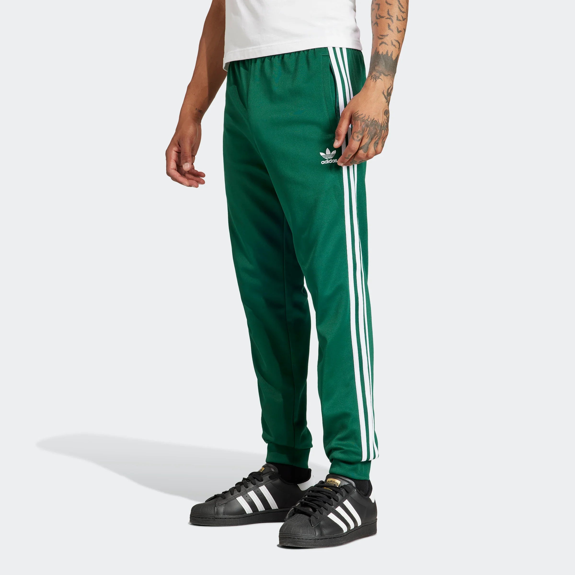 "Adidas Classics SST Track Pants in Dunkelgrün aus Polyester/Baumwolle, schmal geschnitten, klassische adidas Trainingshose mit Streifen bei Stickabush Berlin.“