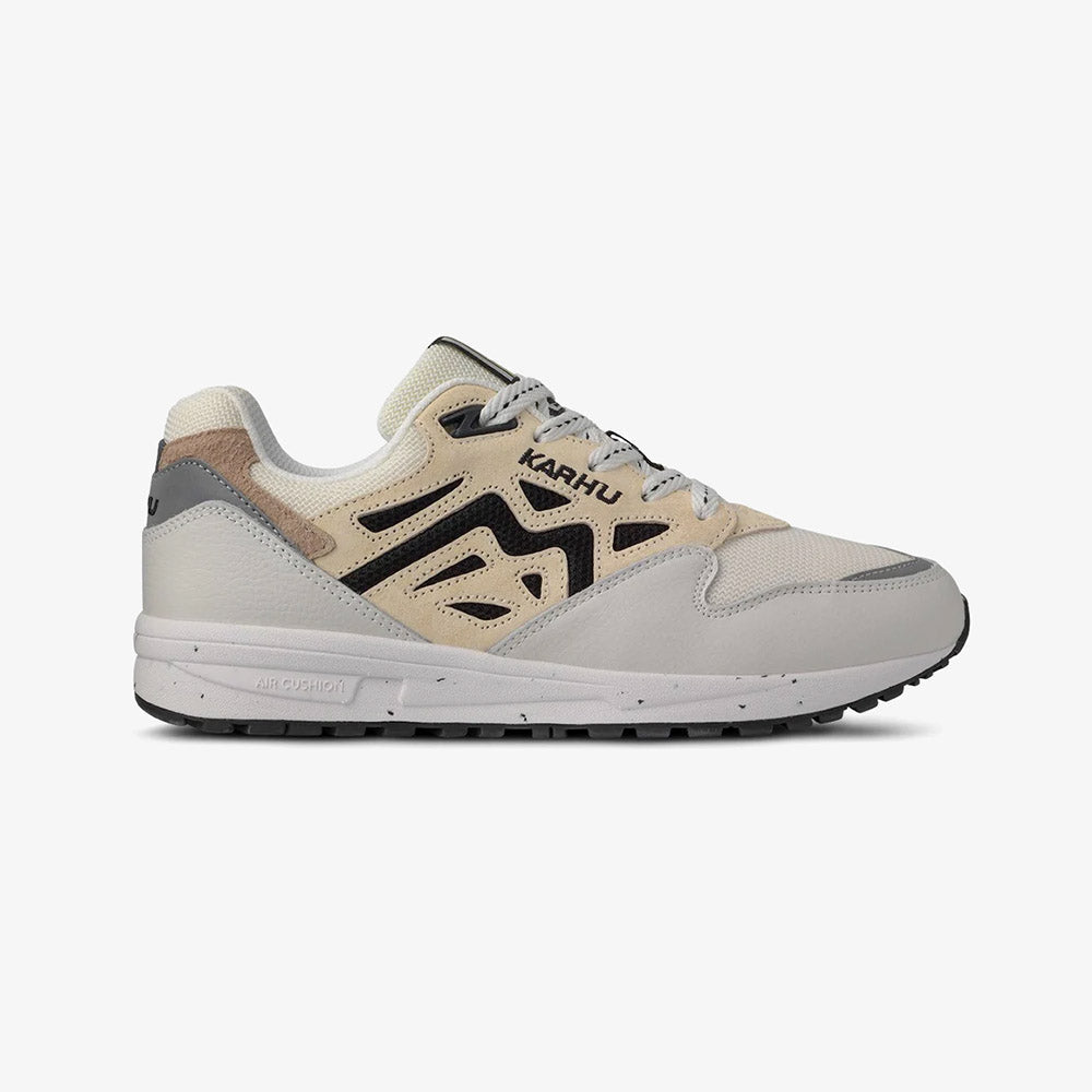 “Die Karhu Legacy 96 - Blanc de Blanc, Sneakers präsentieren sich in einem beigen und hellgrauen Design mit schwarzen Akzenten. Sie verfügen über weiße Schnürsenkel, eine klobige Sohle, einen perforierten Zehenbereich und einen strukturierten Absatz.“