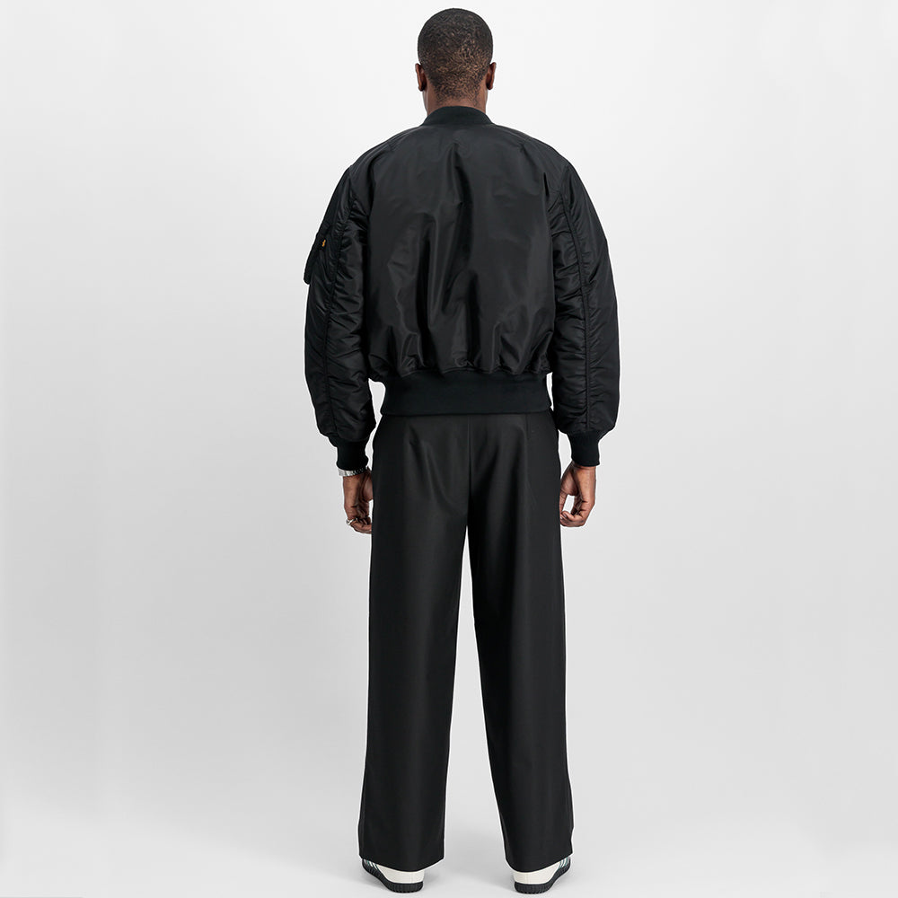 “Alpha Industries MA-1 (HERITAGE) Bomberjacke in Schwarz, aus robustem Nylon, mit ikonischem Flight-Tag am Ärmel und gestepptem orangenem Innenfutter.“