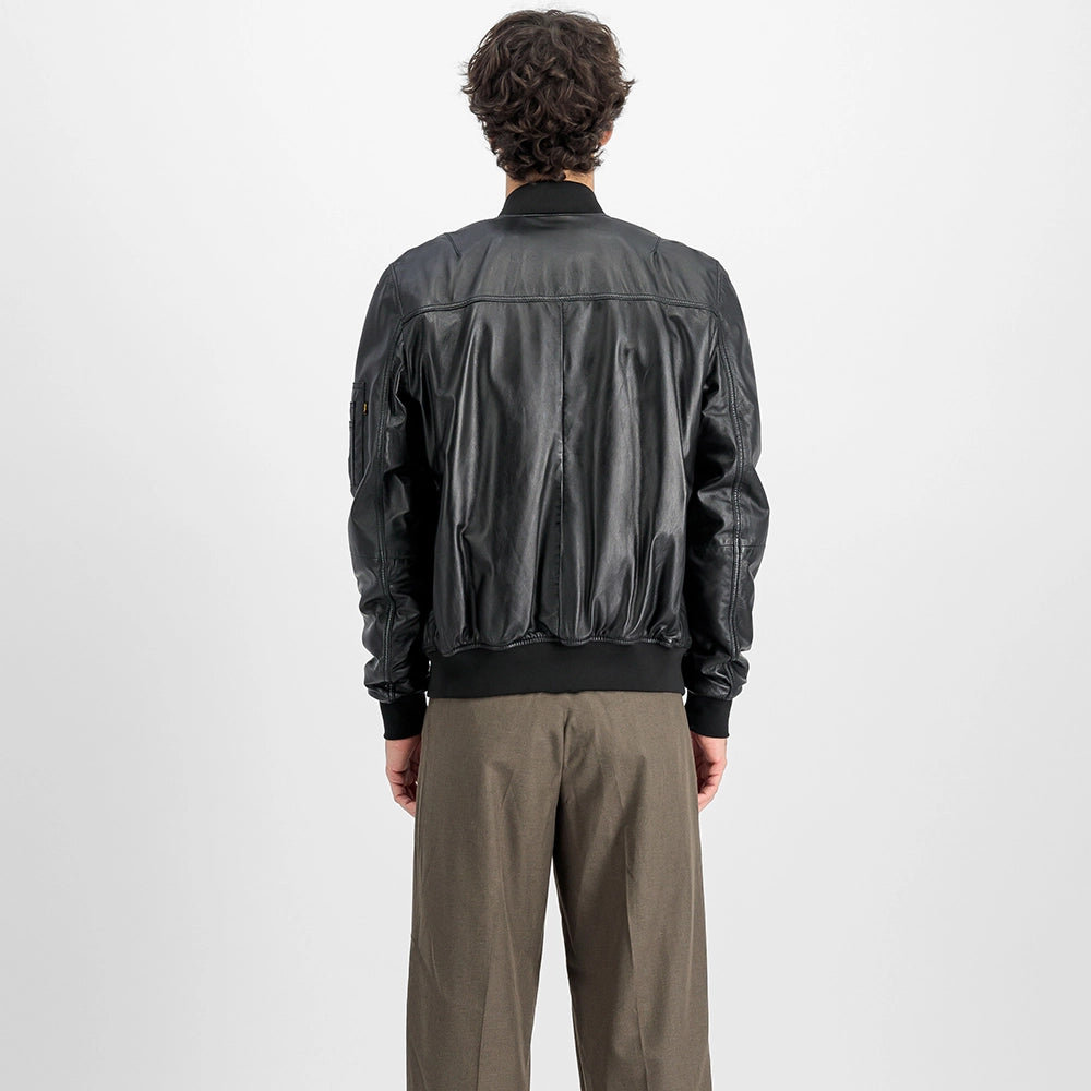 „Schwarze Alpha Industries MA-1 Lederjacke mit Strickkragen, Utility Pocket am Ärmel und rotem Remove Before Flight Tag vor neutralem Hintergrund bei Stickabush Berlin.“