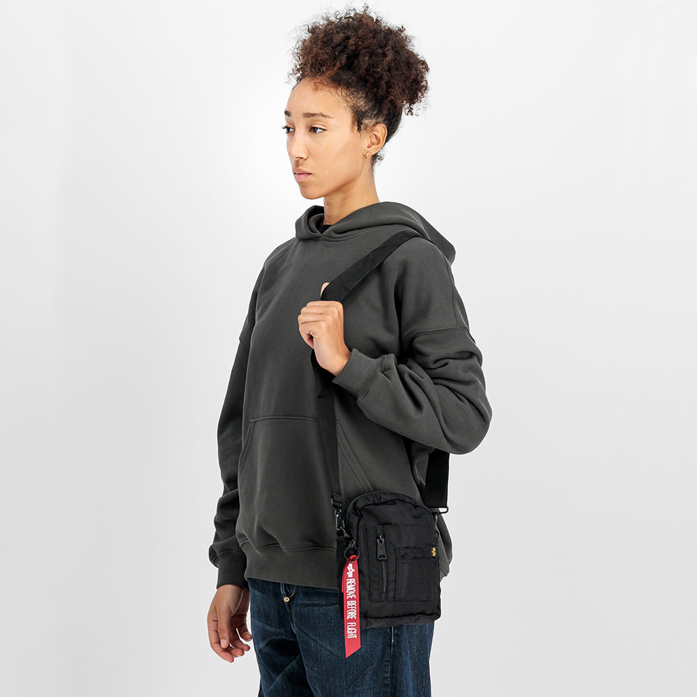 “Alpha Industries Crew Carry Bag – Black. Schwarze Umhaengetasche aus robustem Nylon, mit mehreren Fächern, Tragegriffen und abnehmbarem Schultergurt.“