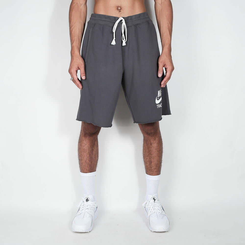 „Nike Sportswear Club Alumni Shorts in Grau/Schwarz mit ungesäumten Kanten, weißem Nike Track & Field Logo-Print und elastischem Bund bei Stickabush Berlin.“