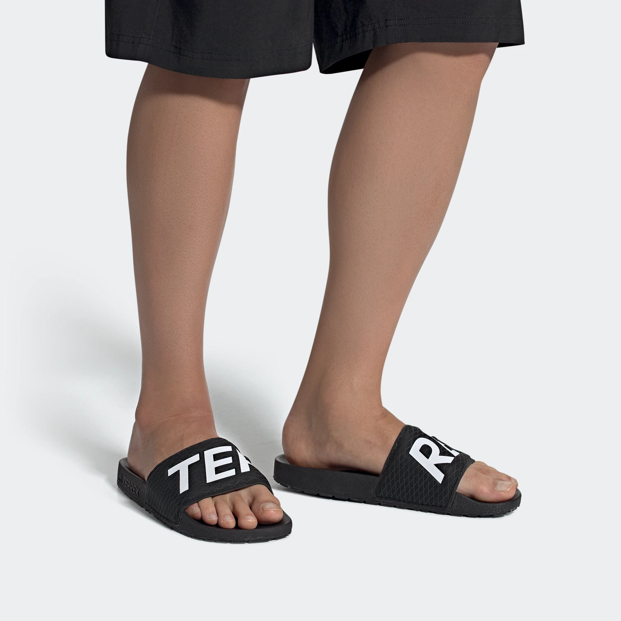 "Schwarze Adidas TERREX Adilette mit weißen Details. Robuste Badesandale mit breitem Riemen und strukturiertem Fußbett für Outdoor-Aktivitäten."