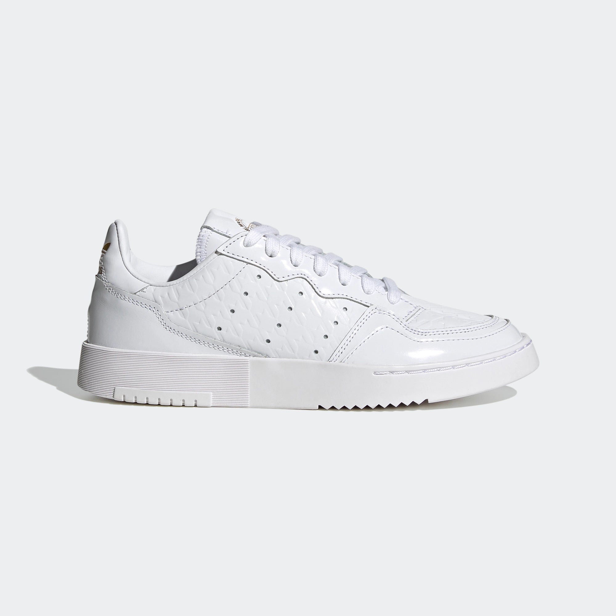 Adidas Supercourt W. Weißer Sneaker aus Leder, mit goldenen Metall-Akzenten, Ziernähten, perforierten 3-Stripes und einer Gummisohle.
