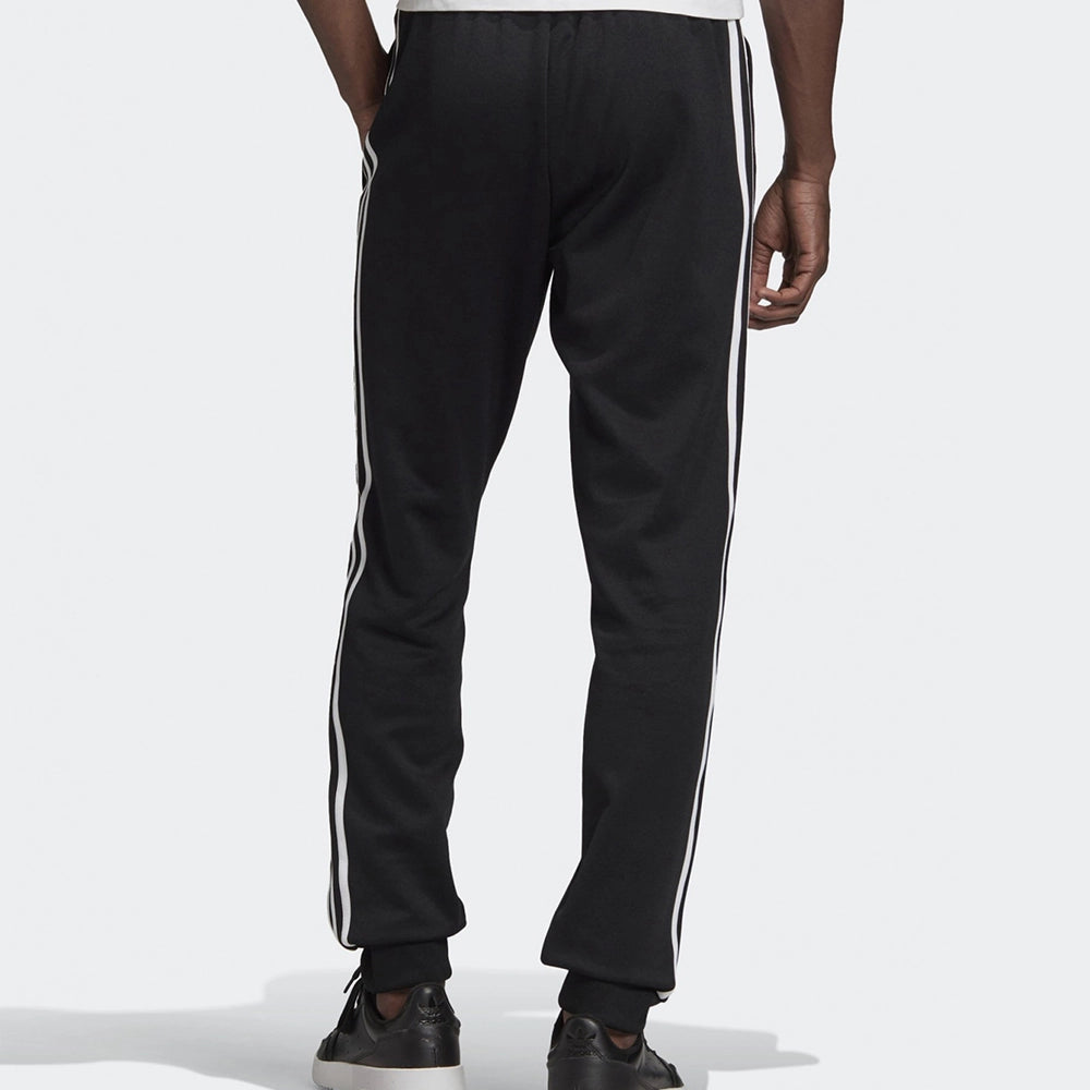 "Schwarze adidas Classics SST Trainingshose mit weißen 3-Streifen, Trefoil-Logo und schmal zulaufendem Bein bei Stickabush Berlin."