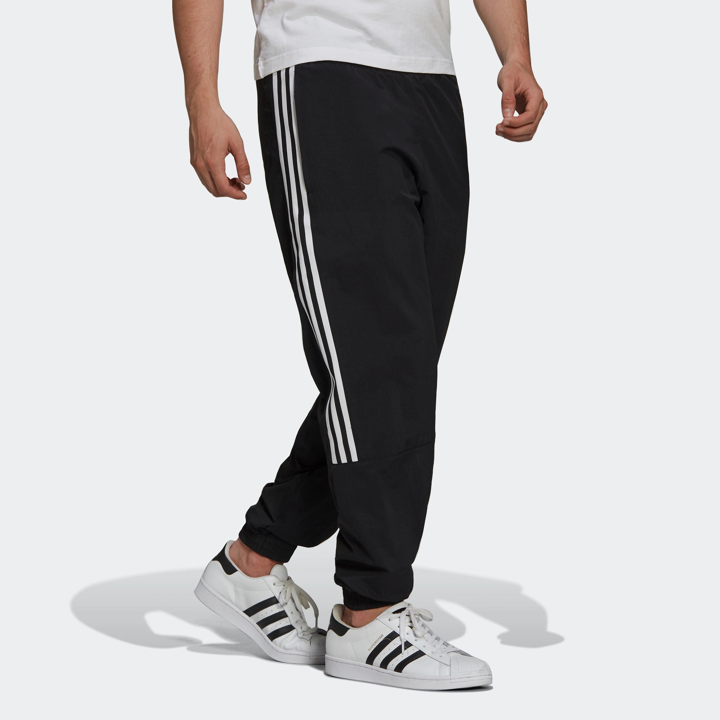 "Schwarze Adidas Trainingshose mit weißen seitlichen Streifen und weißem Trefoil-Logo am Bein. Klassischer Schnitt mit elastischem Bund und Bündchen."