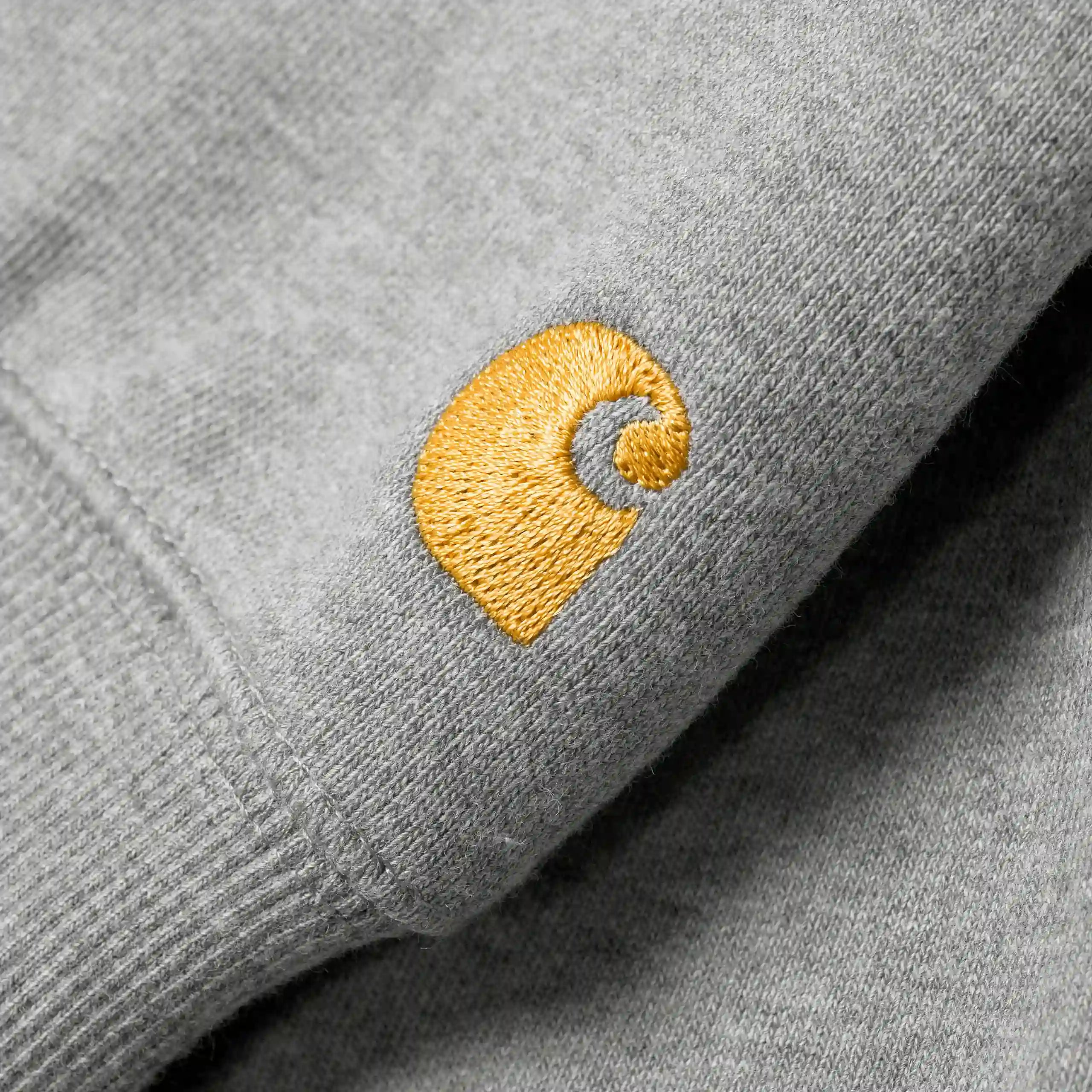 "Detailaufnahme der goldenen Carhartt WIP Logo-Stickerei am Ärmel des grauen Chase Hoodies – Stickabush Berlin Streetwear"
