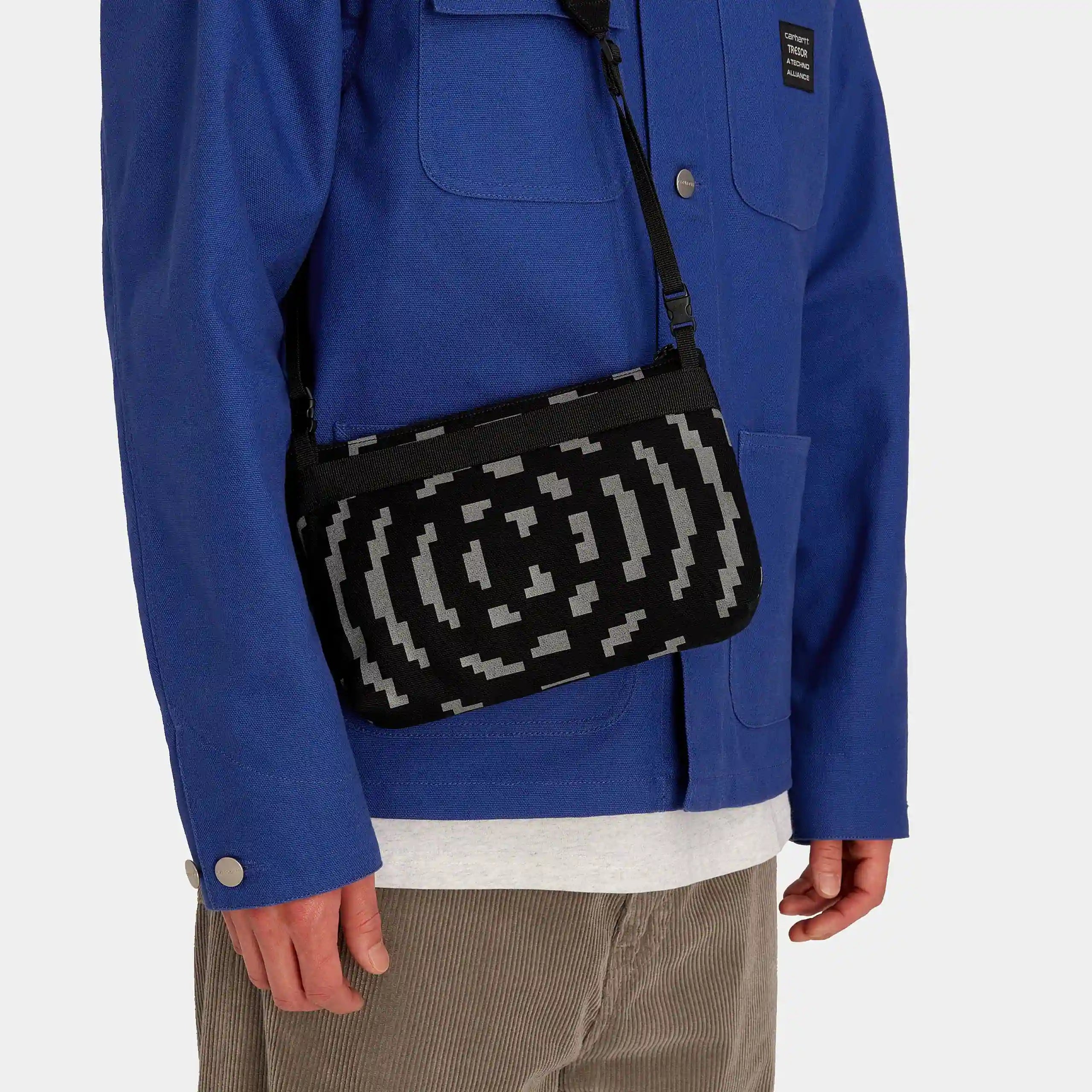 "Carhartt WIP x TRESOR Way Of The Light Strap Bag, Schwarz/Dunkelgrau reflektierend, kleine Umhängetasche mit reflektierenden Details und Logos."