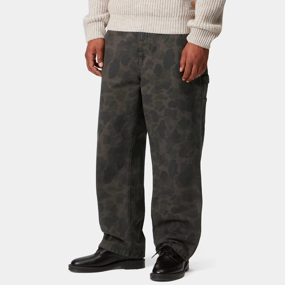 “Carhartt WIP Duck Single Knee Pant in Camo Duck. Robuste Workwear Canvas-Hose in Grün/Porphyr-Färbung mit Werkzeugtaschen und Hammerschlaufe.“
