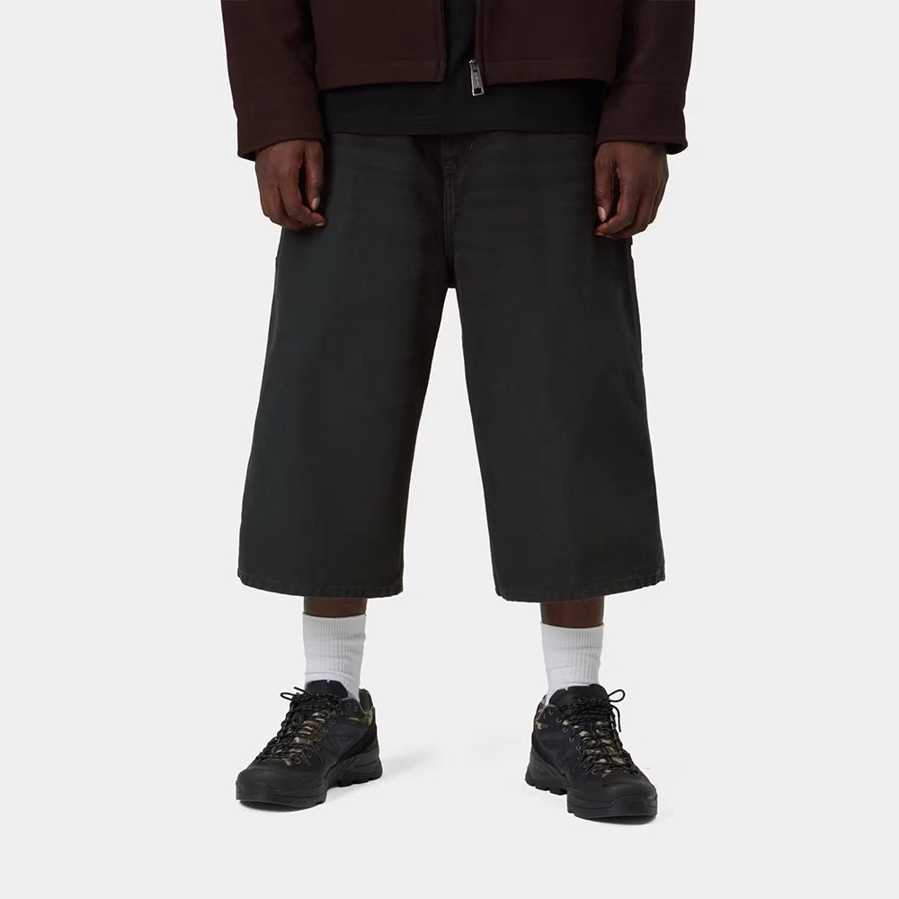 Carhartt WIP OG Single Knee Long Short in Black – Vorderansicht am Model der schwarzen Canvas-Workwear-Shorts mit Tool-Taschen und Hammerlasche.