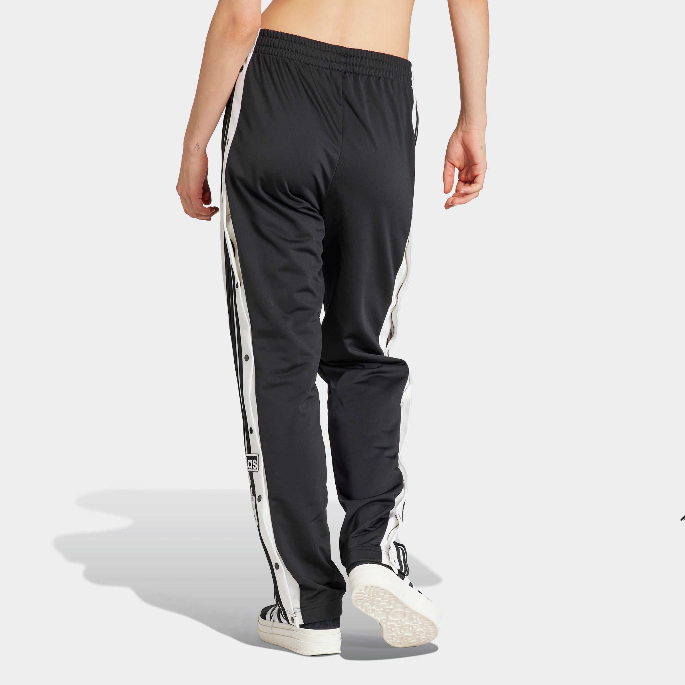 "Schwarze Adidas Adibreak Trainingshose für Damen. Lockere Passform, seitliche Druckknopfleisten, kleines, weißes Adidas Logo am Bein."