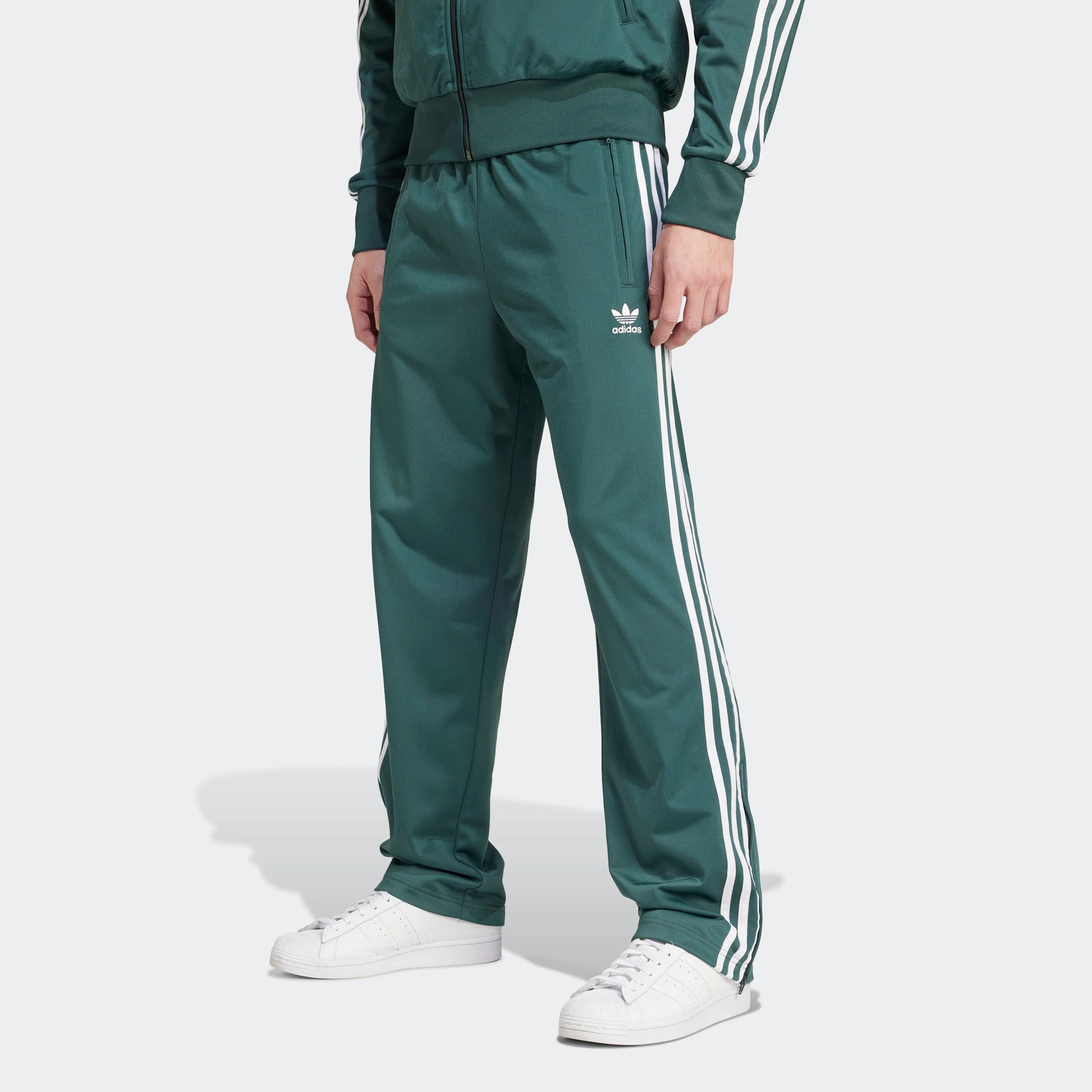 "Adidas Firebird Track Pants in Mineral Green/Weiß, Polyester, klassische Trainingshose mit weißen Streifen, grüne Farbe."