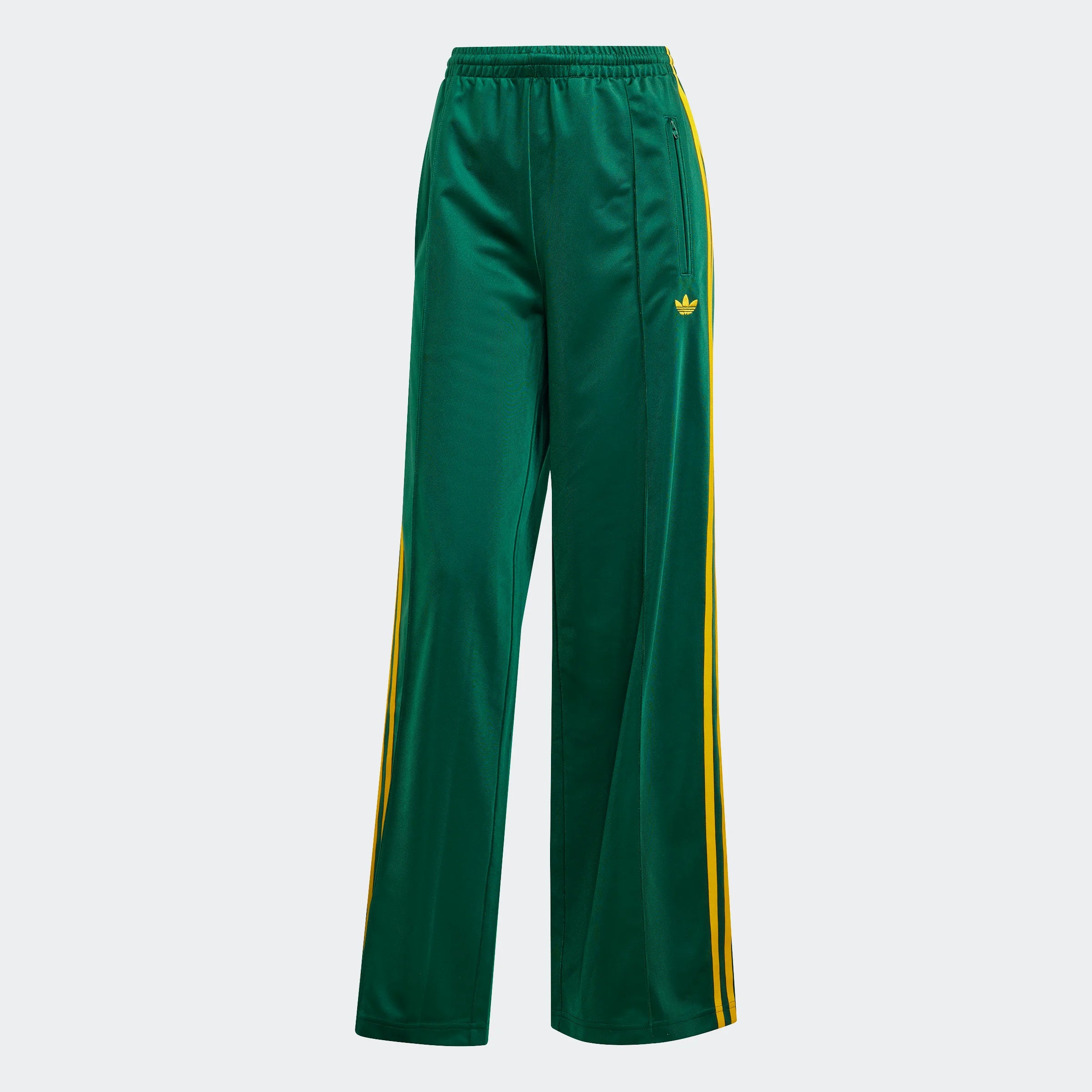 "Grüne Adidas Firebird Trainingshose für Damen mit gelben Streifen. Lockerer Schnitt, glänzendes Trikotmaterial, seitliche Reißverschlusstaschen und kleines Logo."
